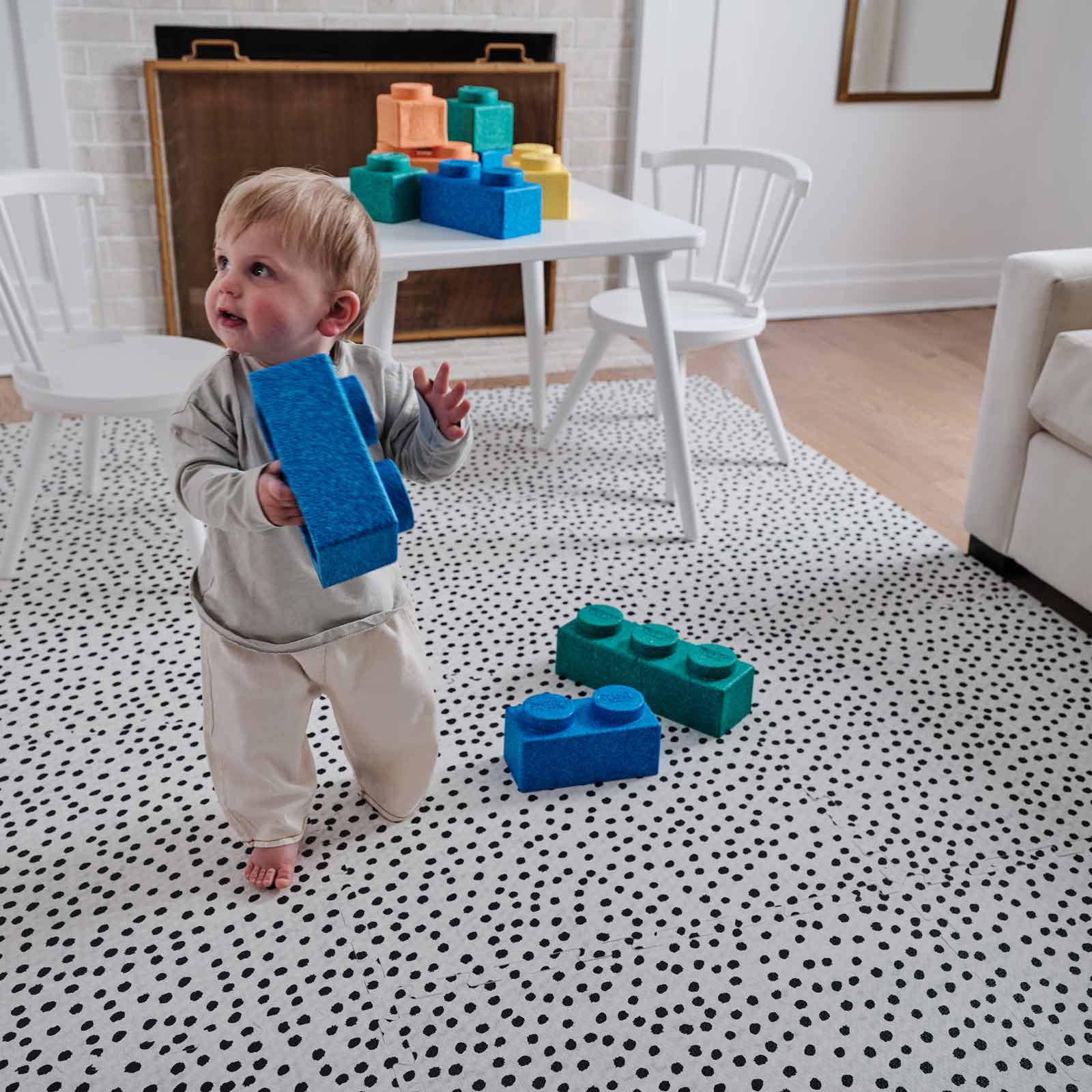 Apollo Pepper black and white spotted pattern play mat shown in living room with toddler boy carrying giant lego blocks