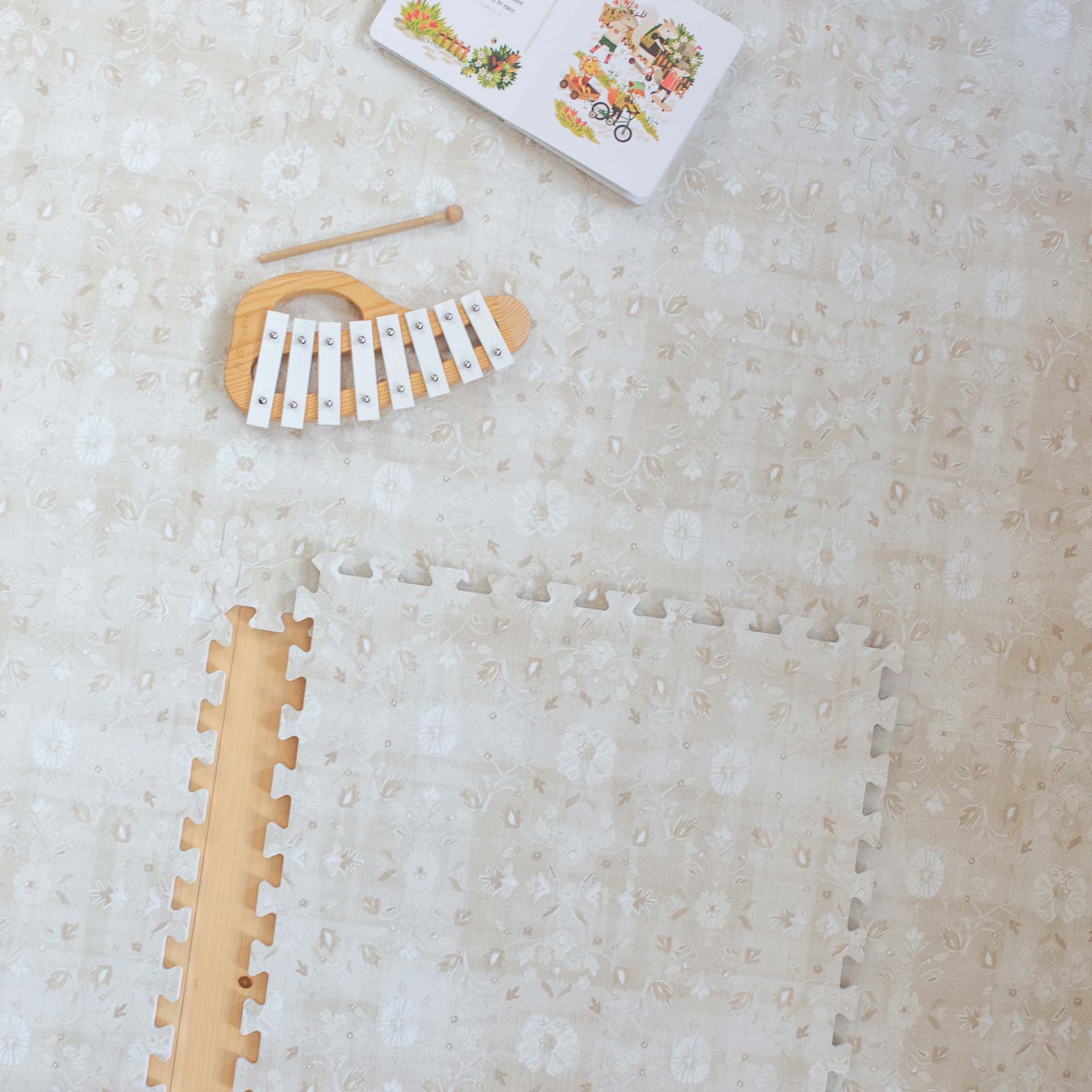 Gemma Chateau neutral floral play mat shown from above with 1 tile exposed and xylophone and book on the mat