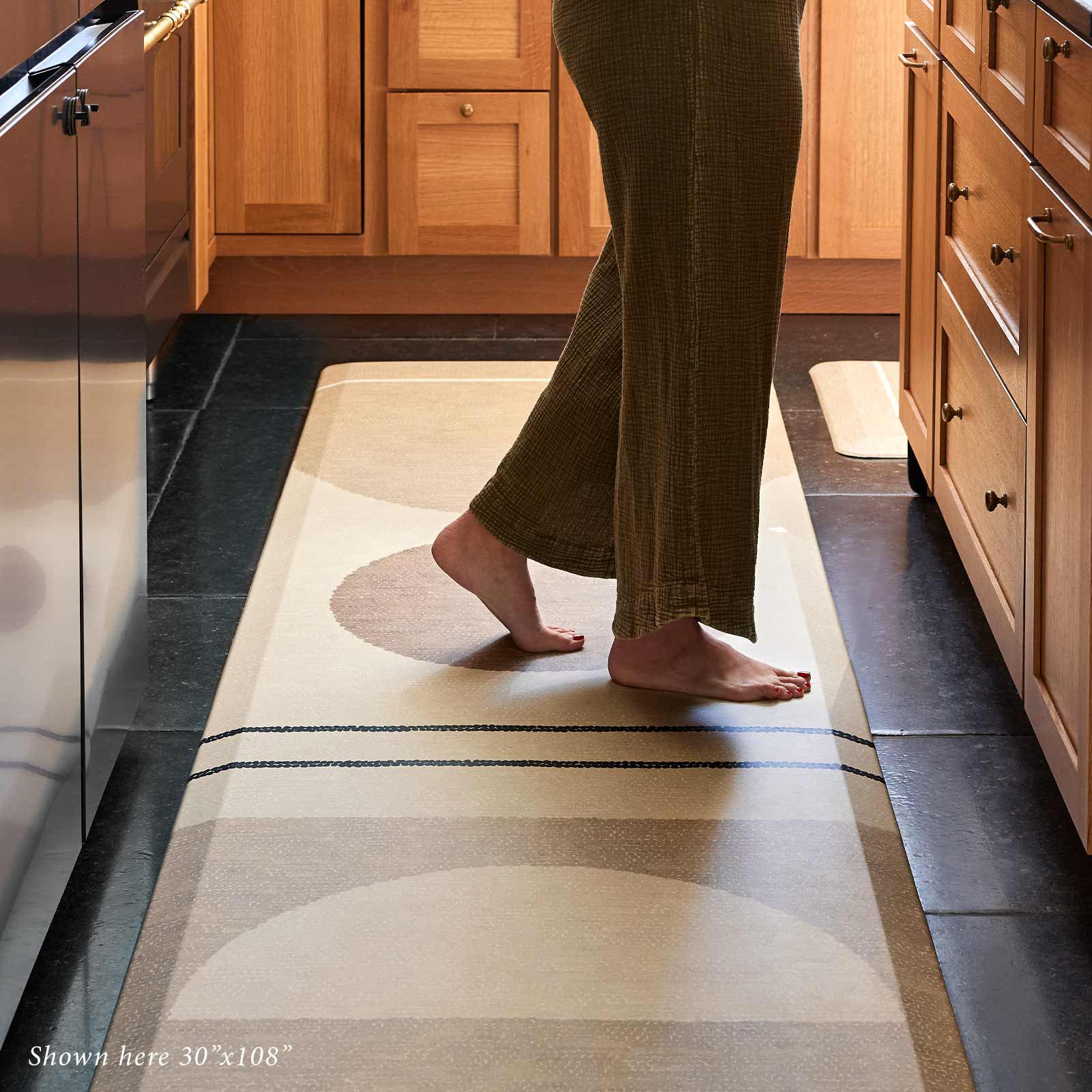 Geode Sesame beige, tan, and brown geometric line print standing mat in size 30x108 with woman's feet standing on the mat in front of a kitchen counter