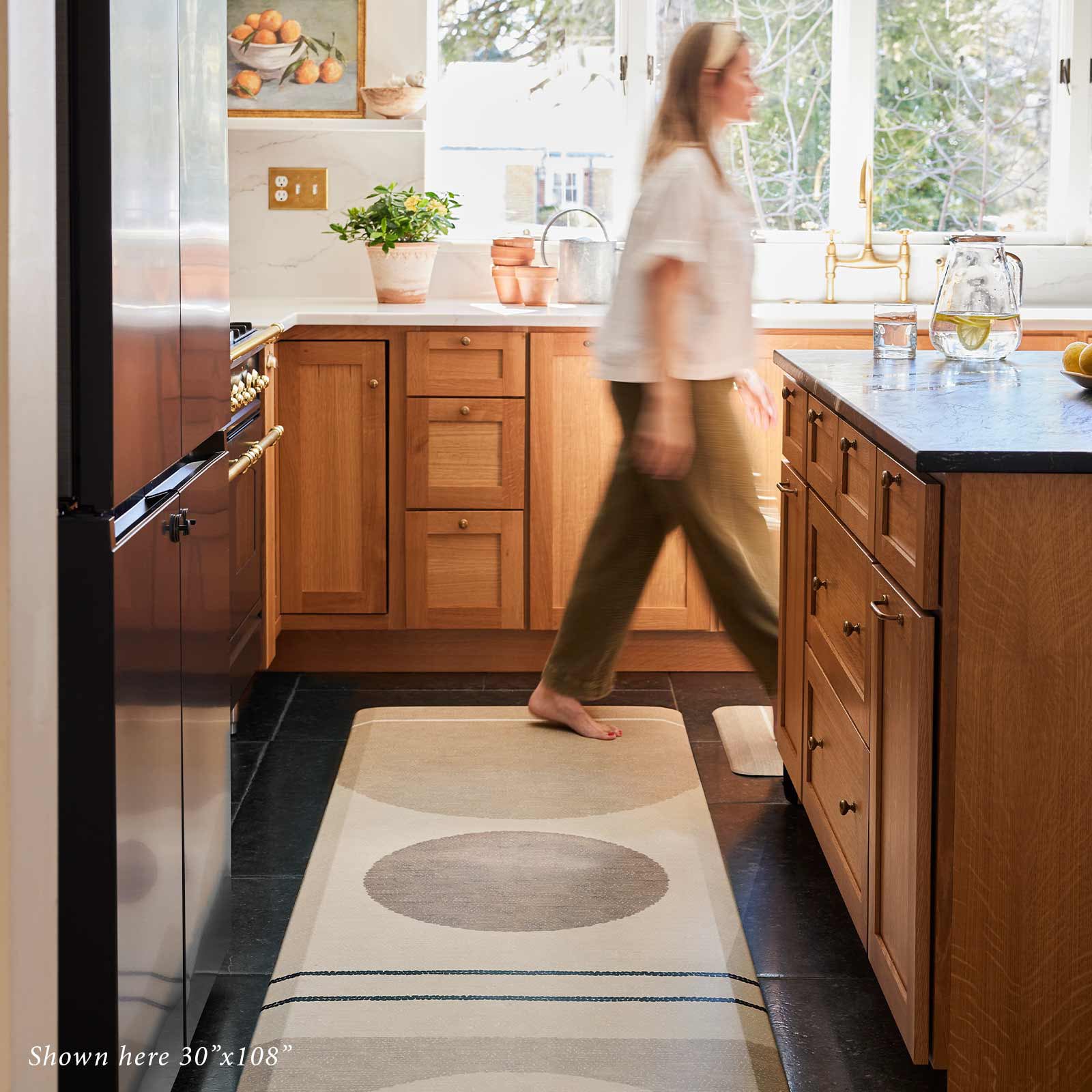 Geode Sesame beige, tan, and brown geometric line print standing mat shown in size 30x108 in front of kitchen island with woman walking past