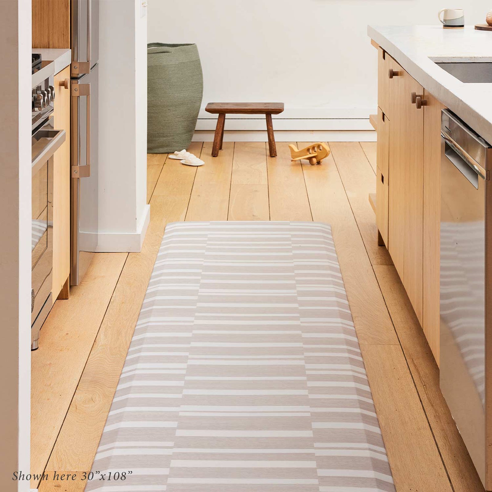 Sutton stripe palomino beige and white inverted stripe standing mat shown in size 30x108 in a light wood tone kitchen in between the counter and island