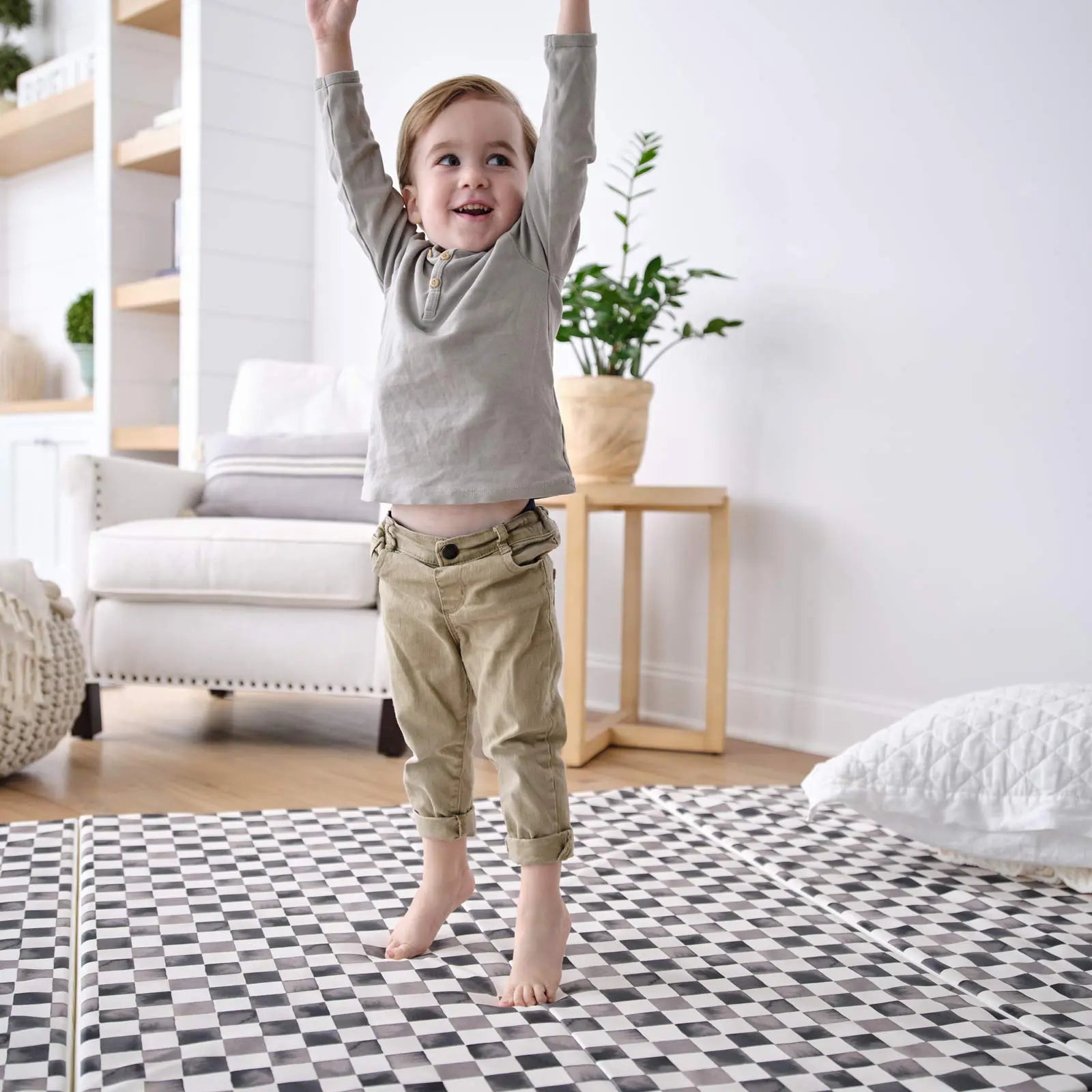 Tuxedo black and white checker print tumbling mat with toddler boy jumping on the mat with his hands up