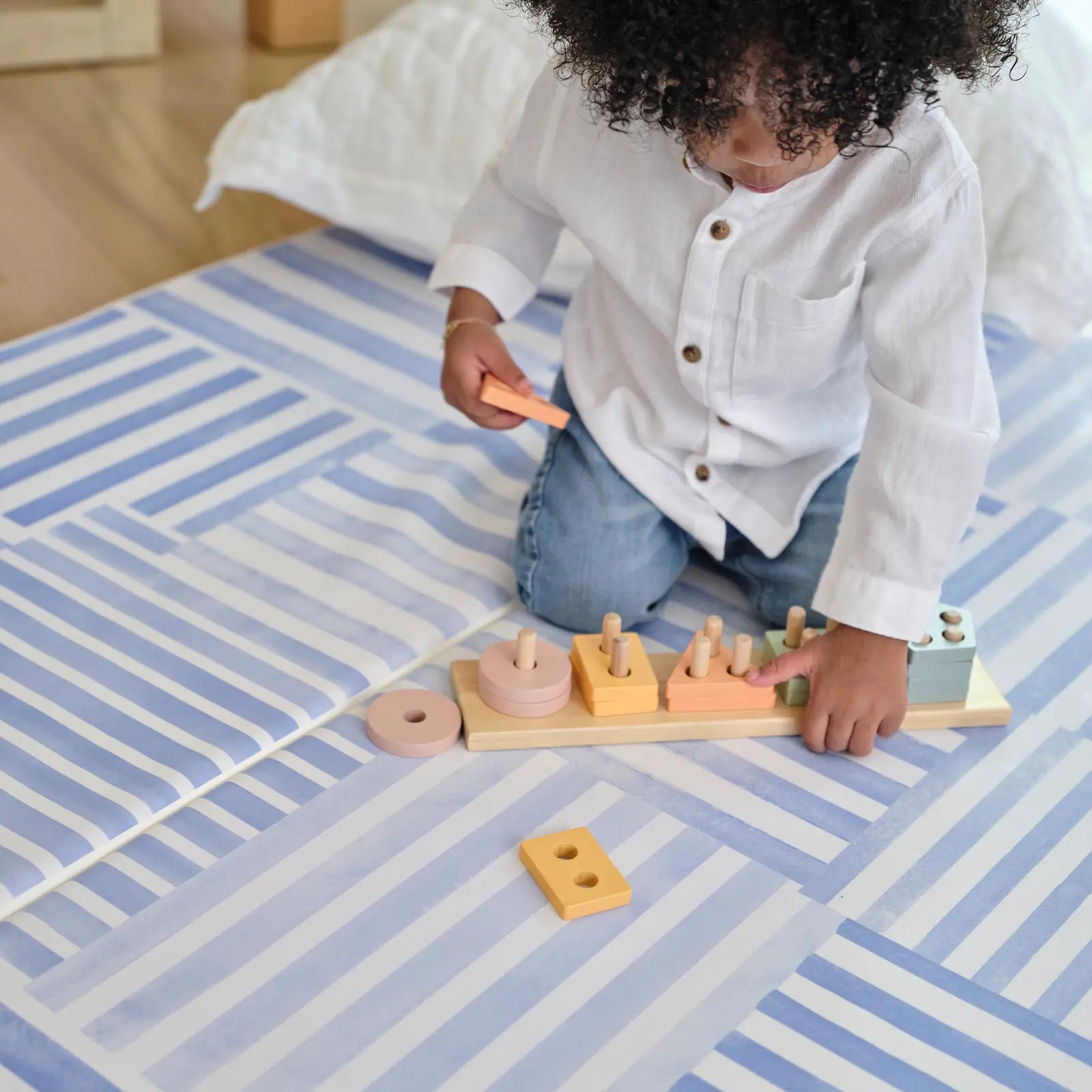 French blue and white inverted stripe tumbling mat shown with toddler playing with rainbow wooden toy on the mat with a pillow behind him