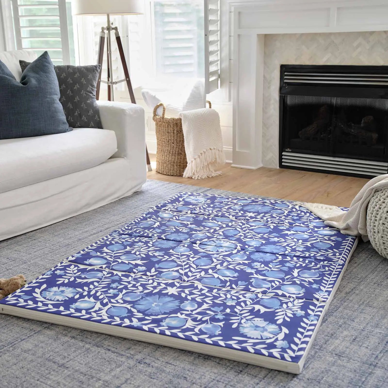 Deep sea blue and white floral tumbling mat shown in living room in front of a couch with blanket, pouf, and plush toy on the floor