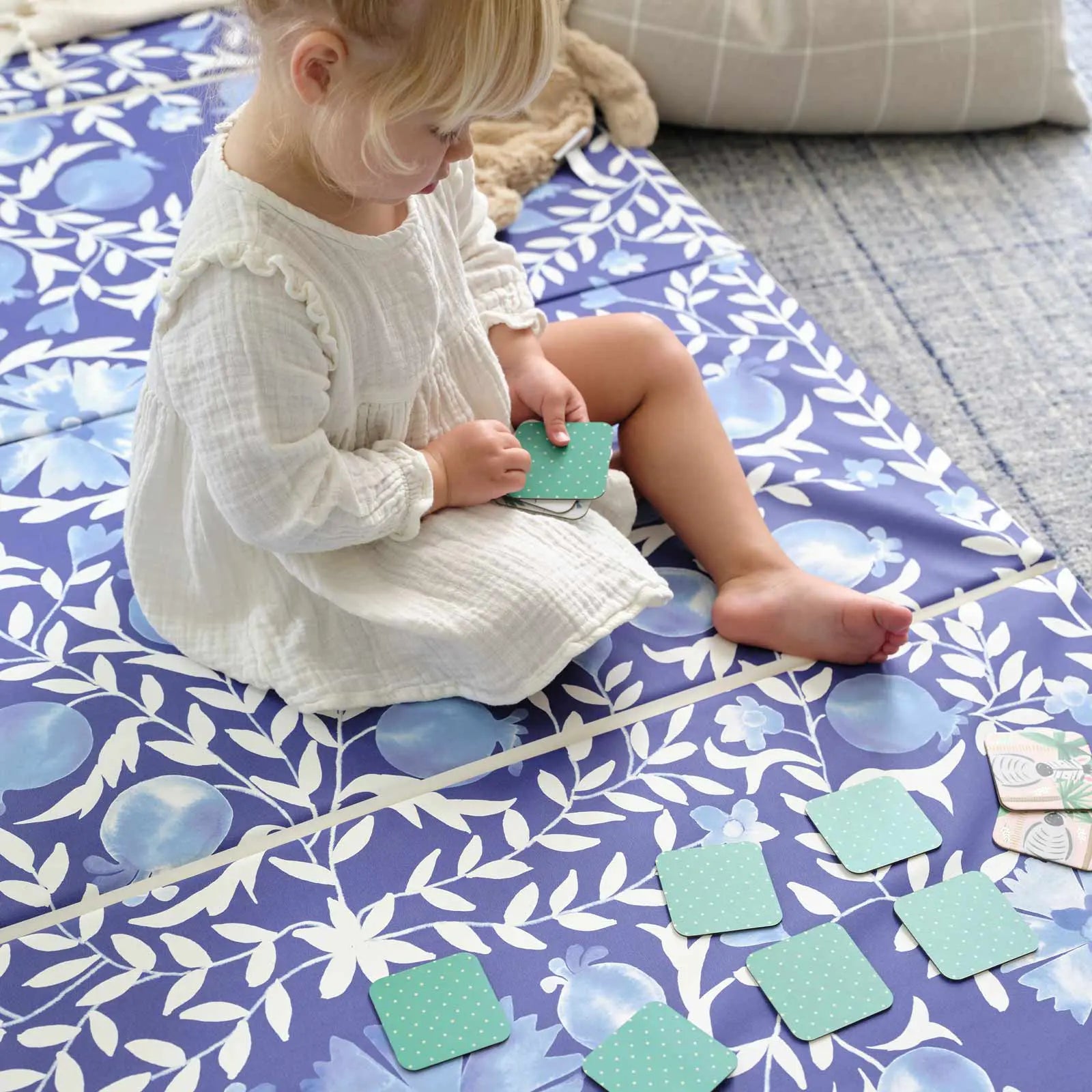 Deep sea blue and white floral tumbling mat shown with toddler girl sitting on the mat playing a memory card game