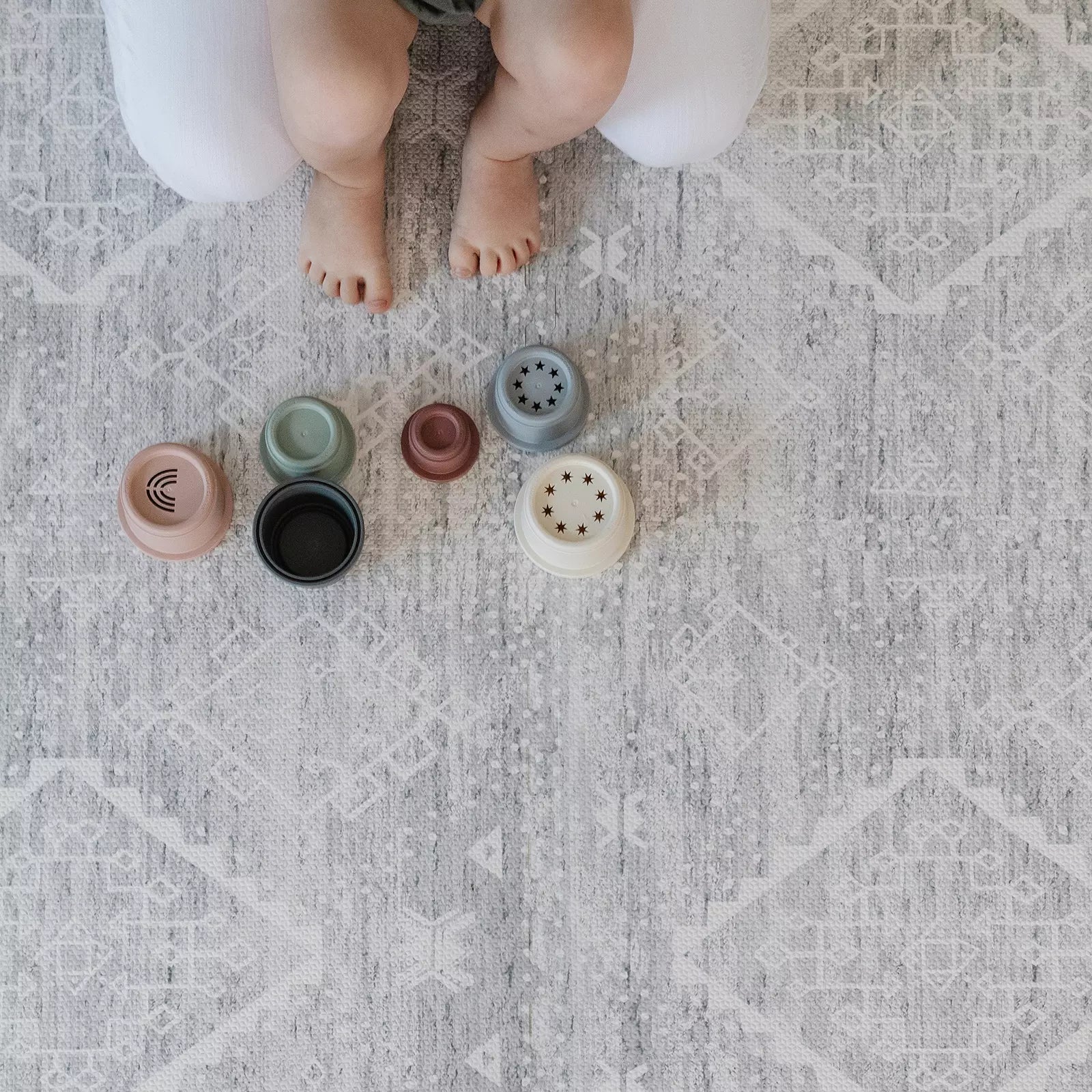 Gray and white minimal boho baby play mat with babies feet hanging off of moms lap and baby toys