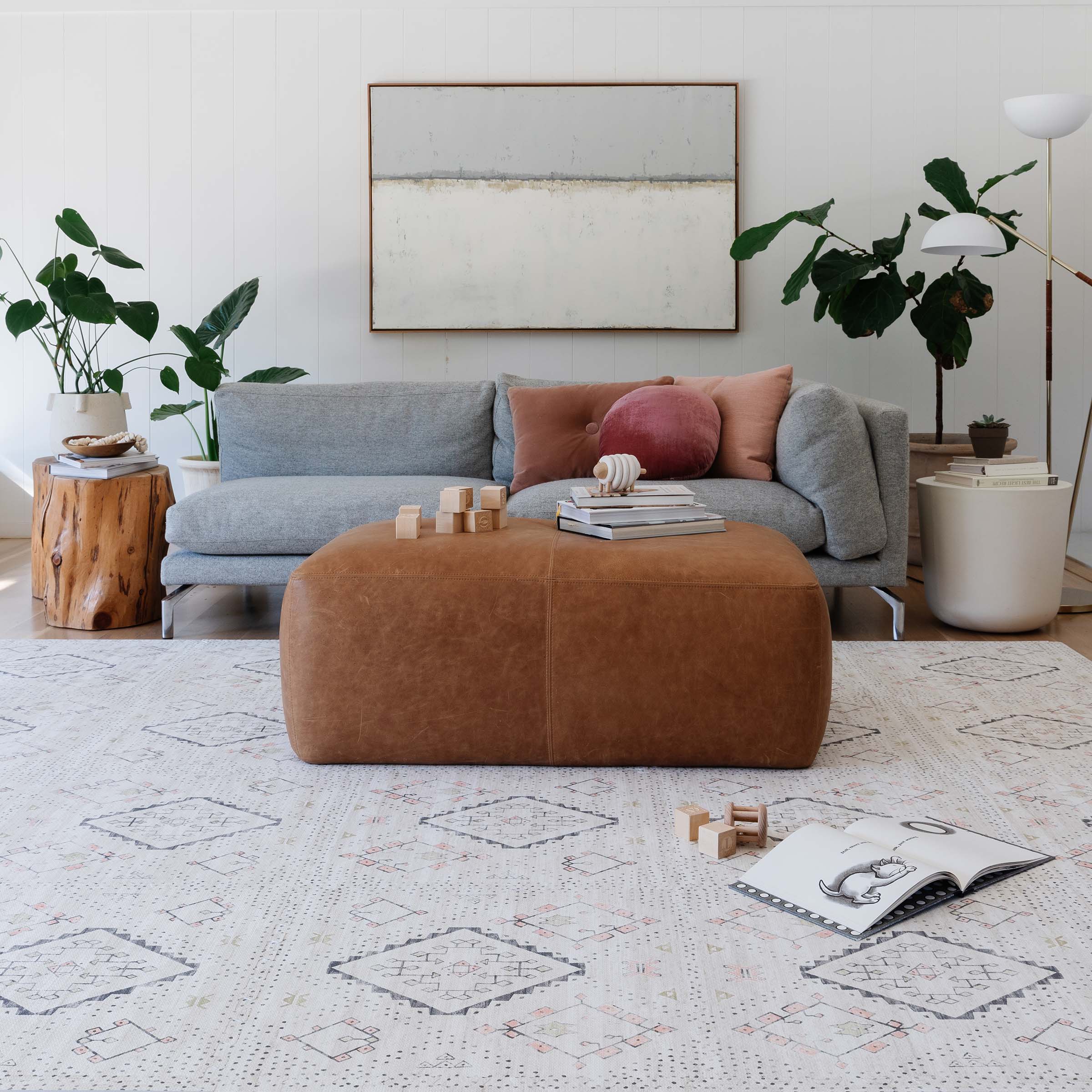 Modern living room with a boho print play mat, gray sofa, brown ottoman, and decorative items.