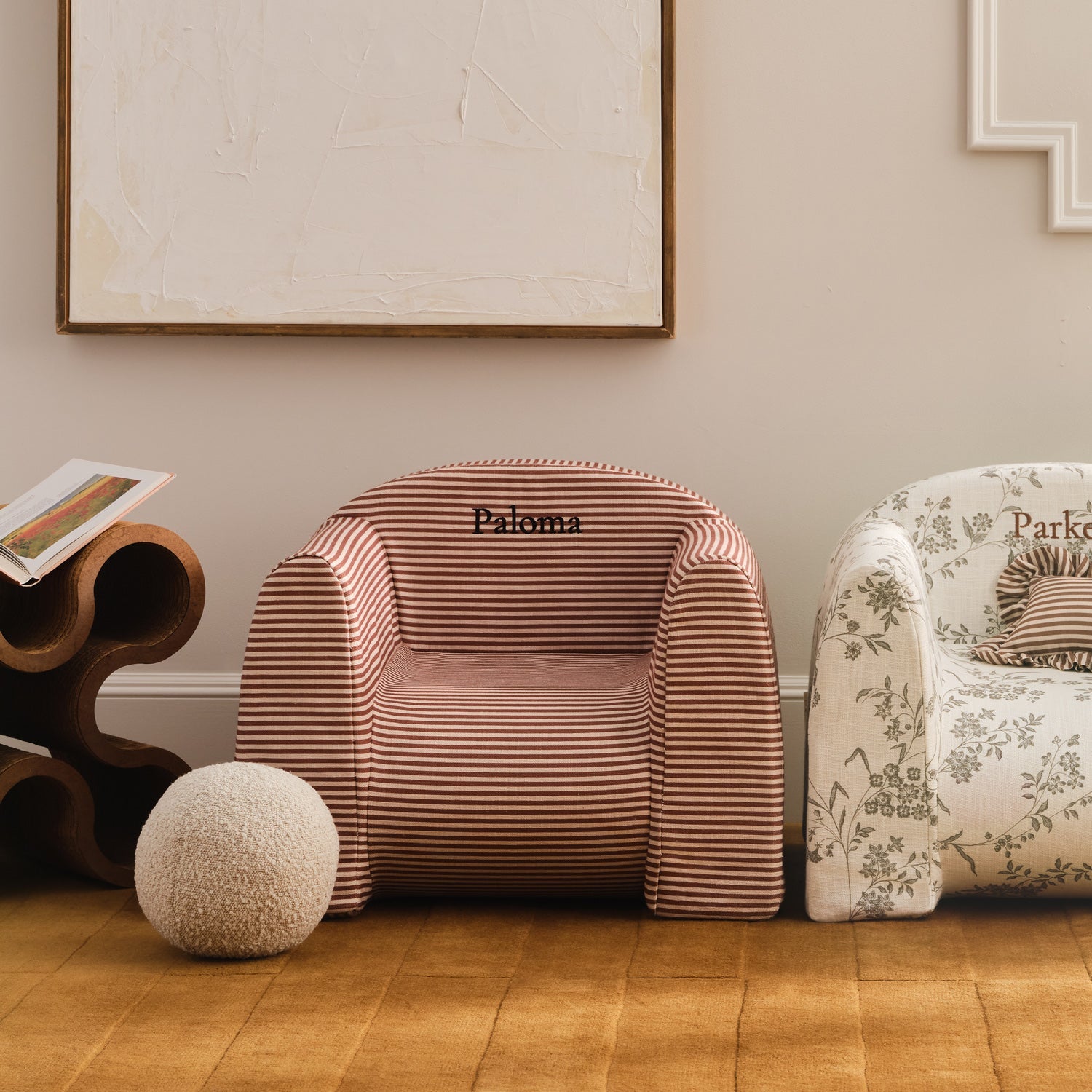 Two armchairs, one striped and one floral, in a room with a wooden floor and framed artwork on the wall.