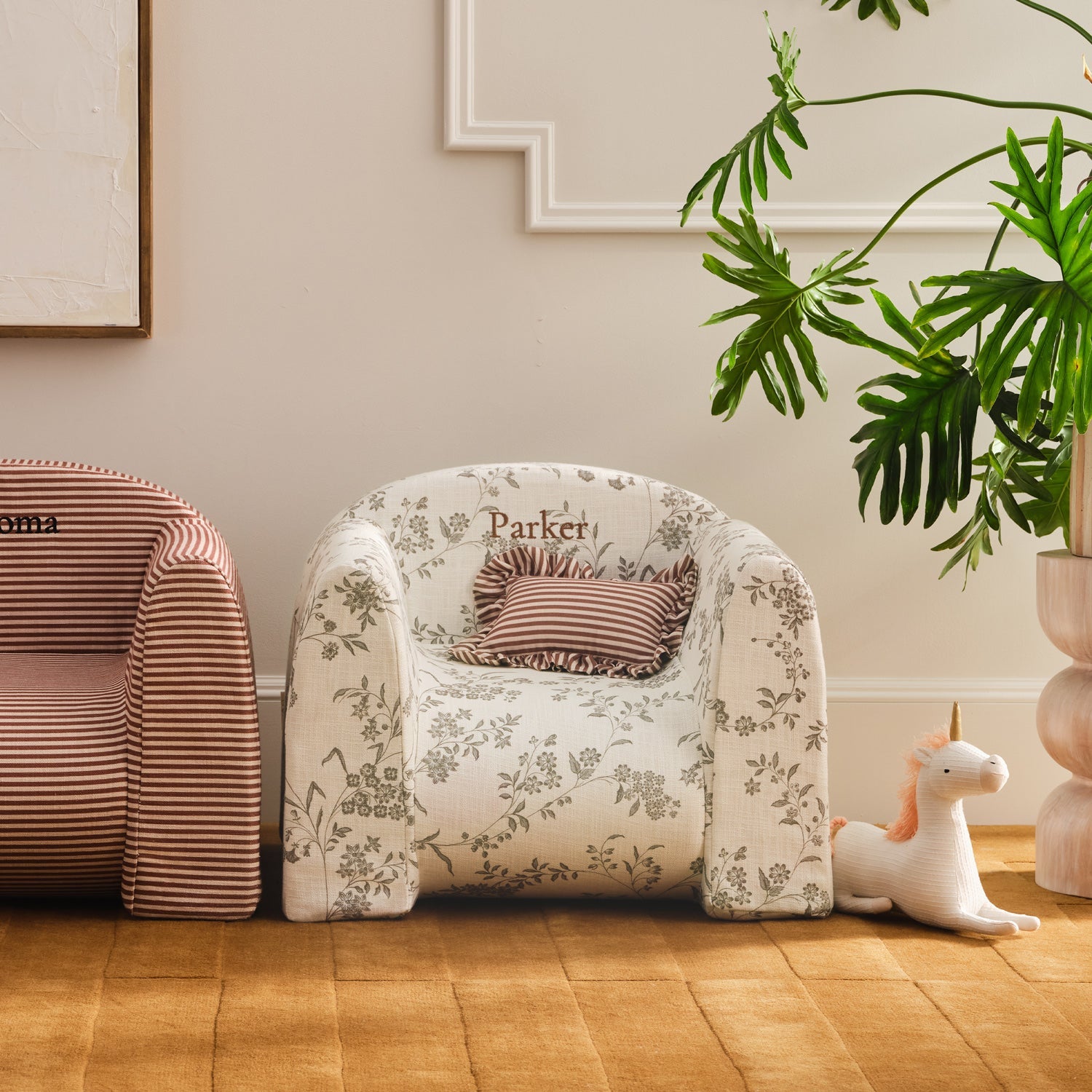 Children's armchair with floral pattern and striped cushion, accompanied by a plant and toys in a room.