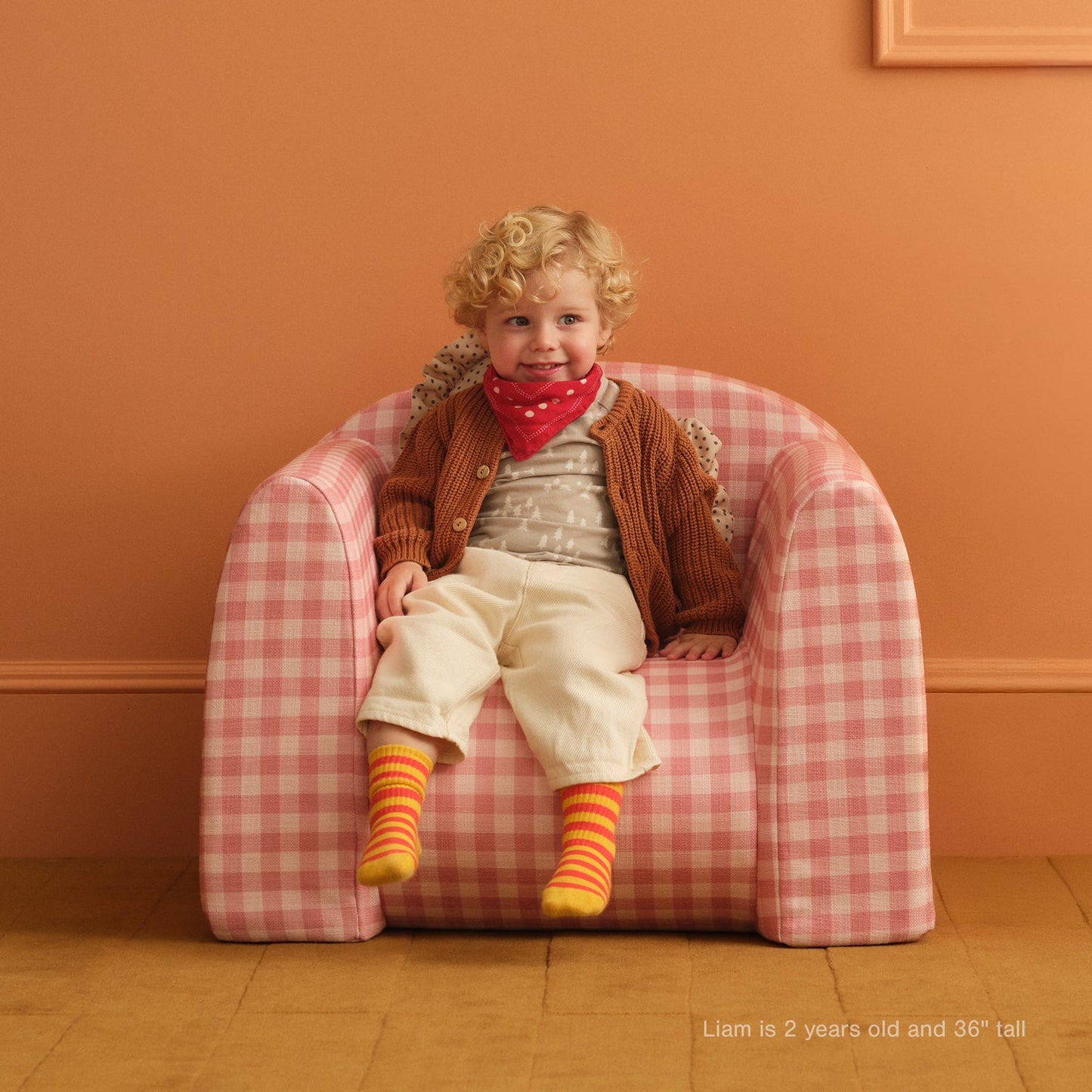 Child sitting on a pink checkered chair against an orange wall
