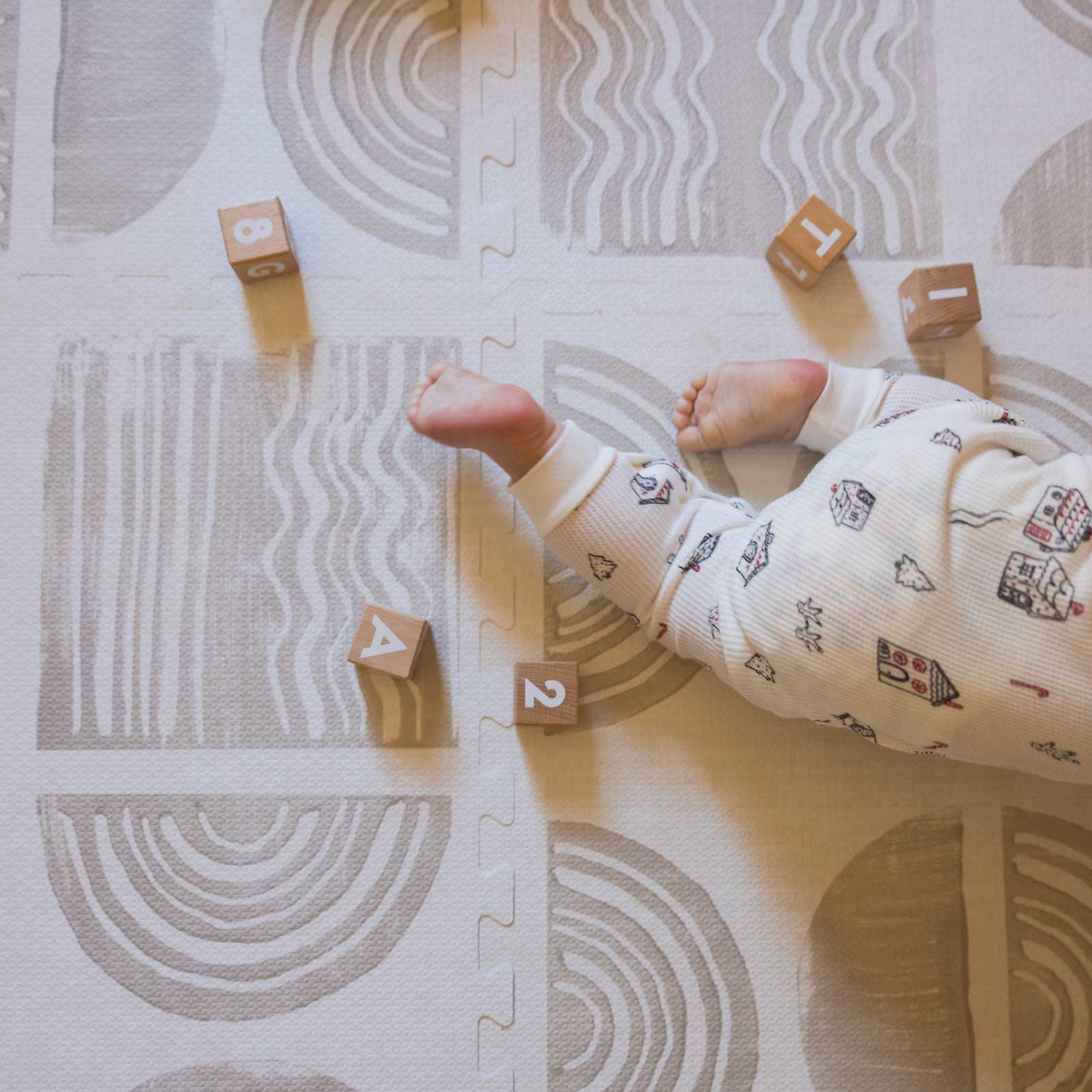 Ada pebble neutral geometric print play mat with wooden blocks and baby wearing christmas pajamas crawling out of the shot