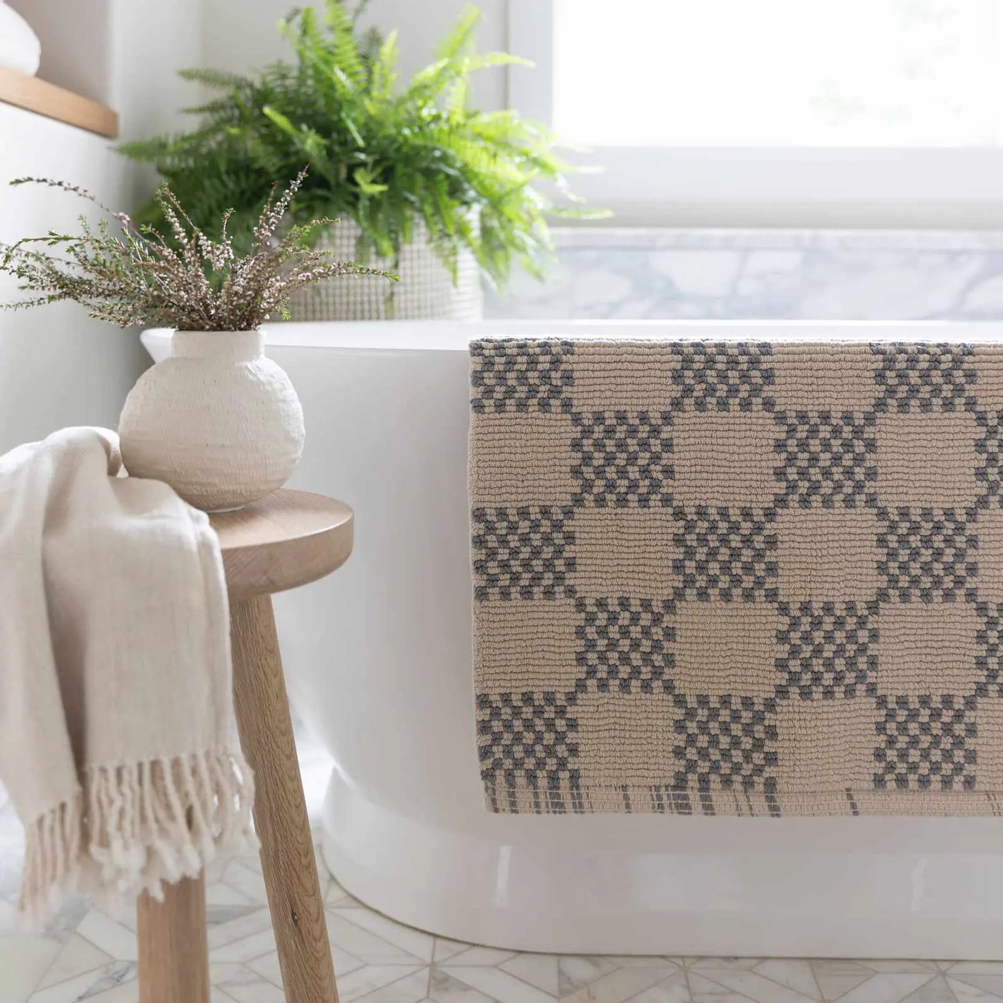 Bath mat in checker harbor gray print in size 21x34 hanging over the edge of a bath tub