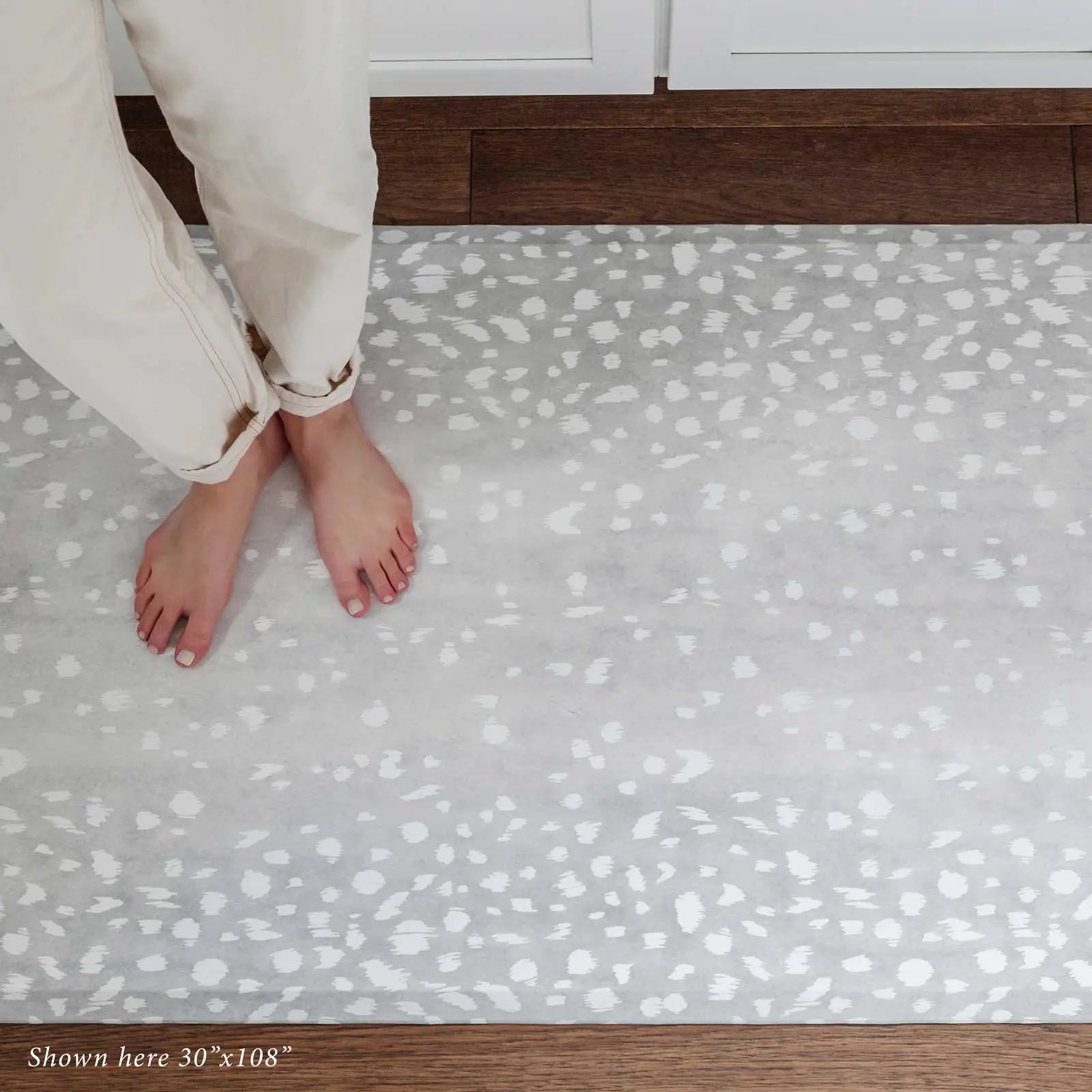 Fawn silver gray animal print kitchen mat shown in size 30x108 with woman's feet standing on the mat