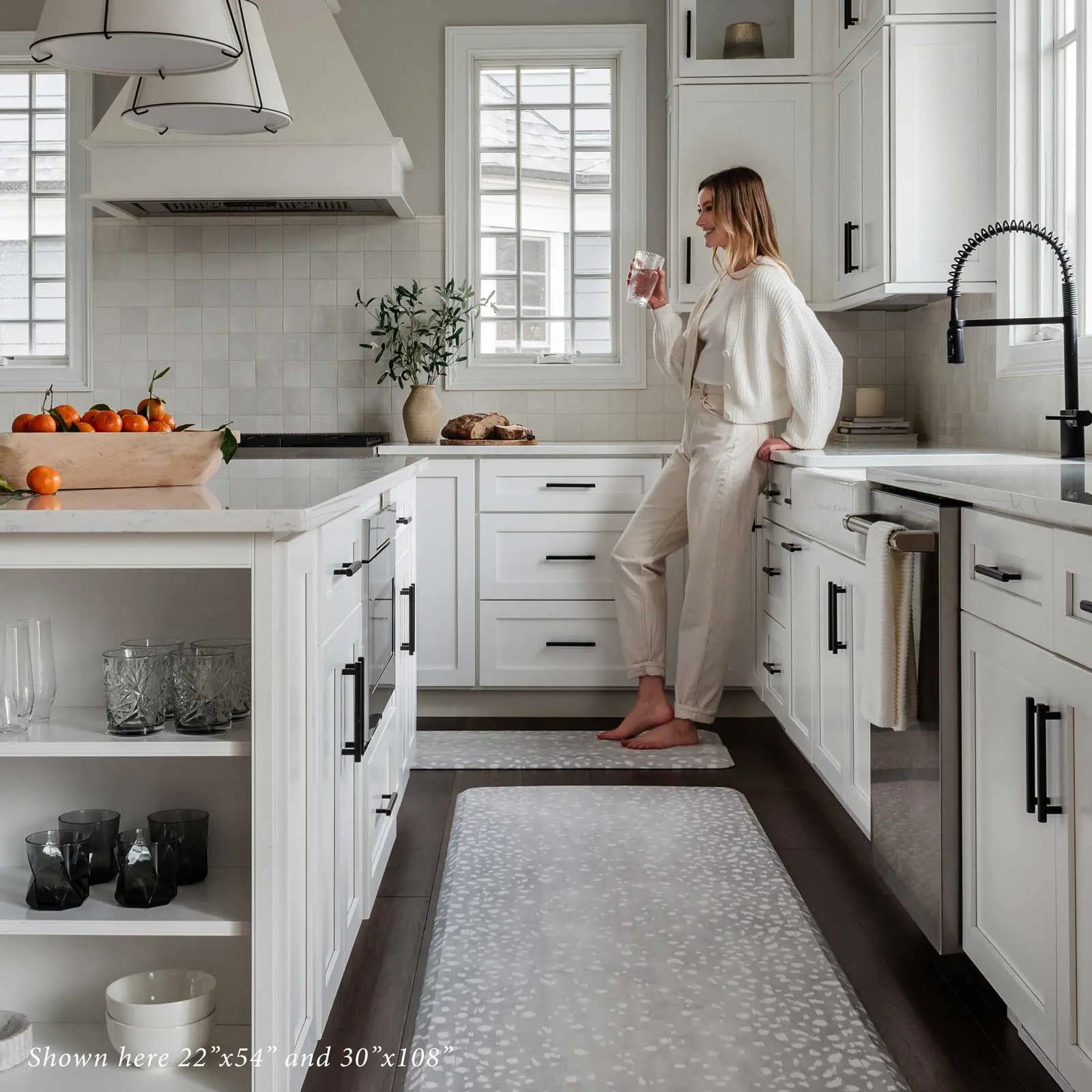 Fawn silver gray animal print standing mat shown in sizes 22x54 and 30x108 in kitchen with woman drinking water 