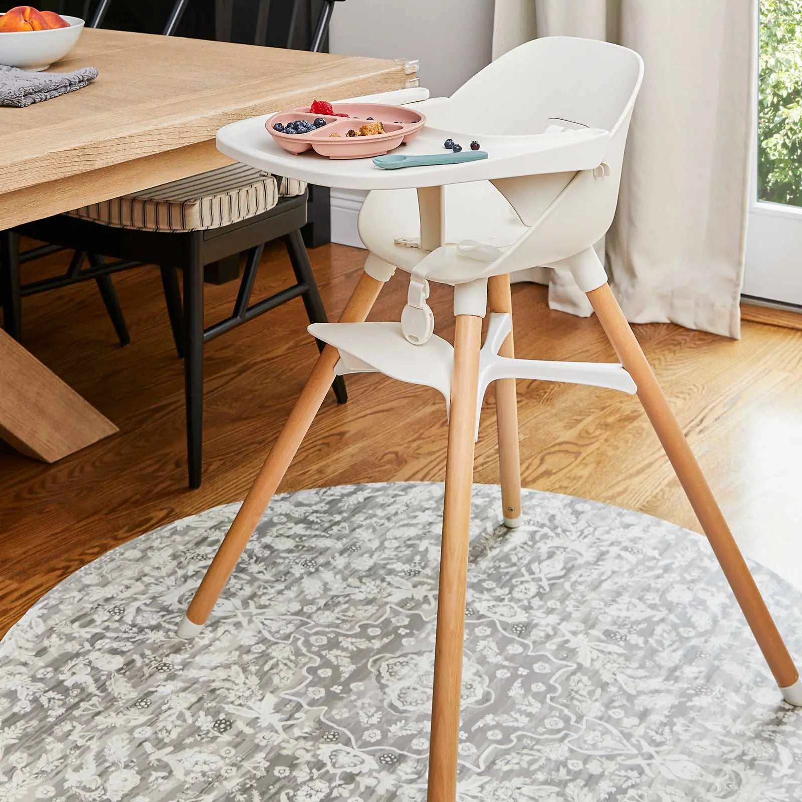 Emile earl grey neutral grey and white vintage floral print high chair mat shown next to dining room table under a high chair with food on the tray