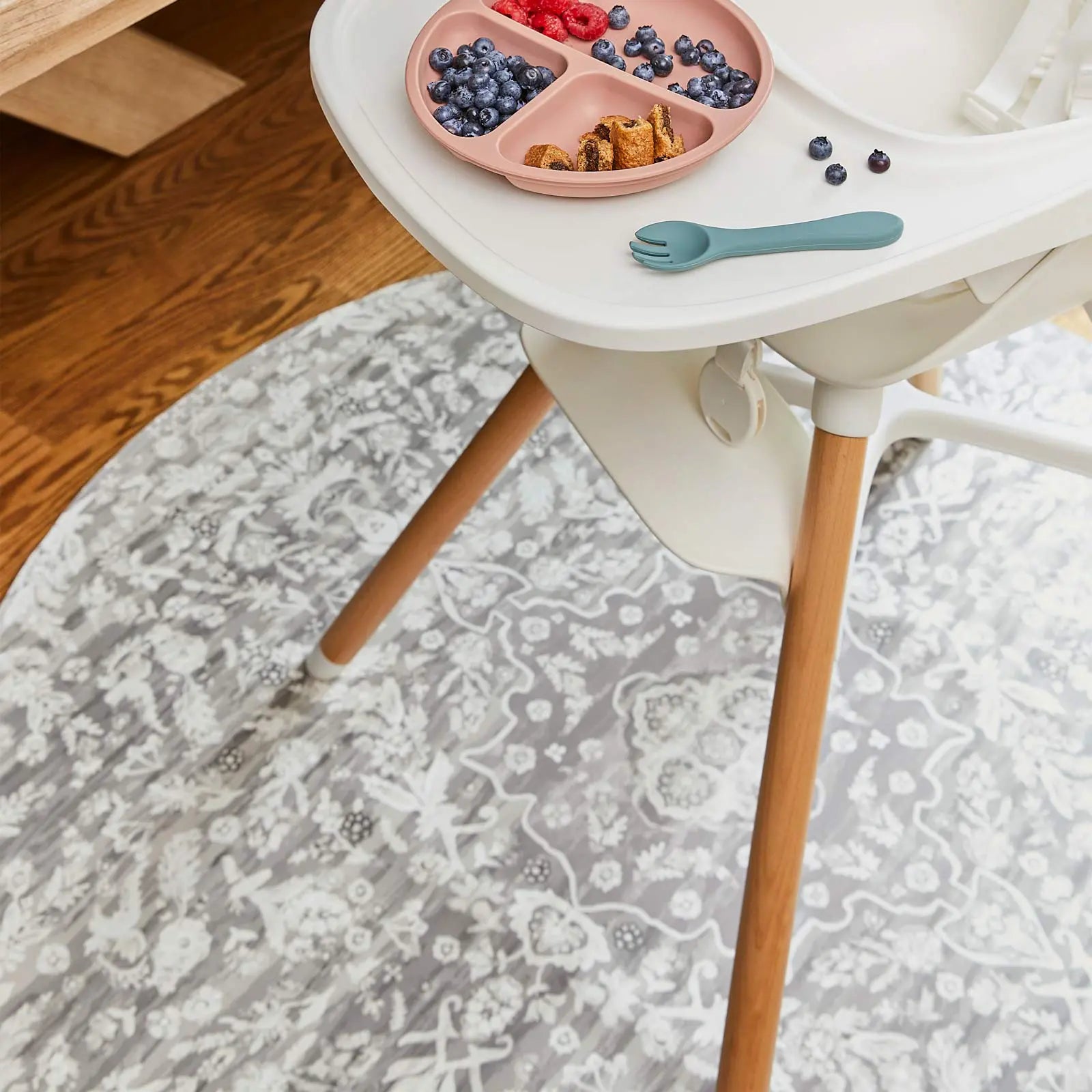 Emile earl grey neutral grey and white vintage floral print high chair mat shown underneath a highchair with fruit and cookies on the tray