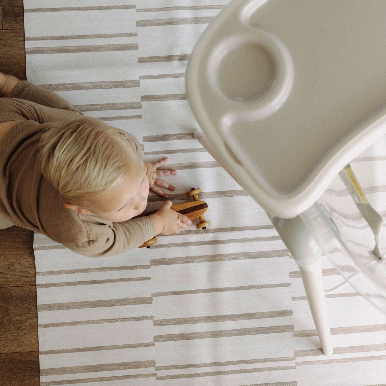 Nara Natural highchair mat shown from above with high chair mat and baby boy crawling across with wooden toy in his hand