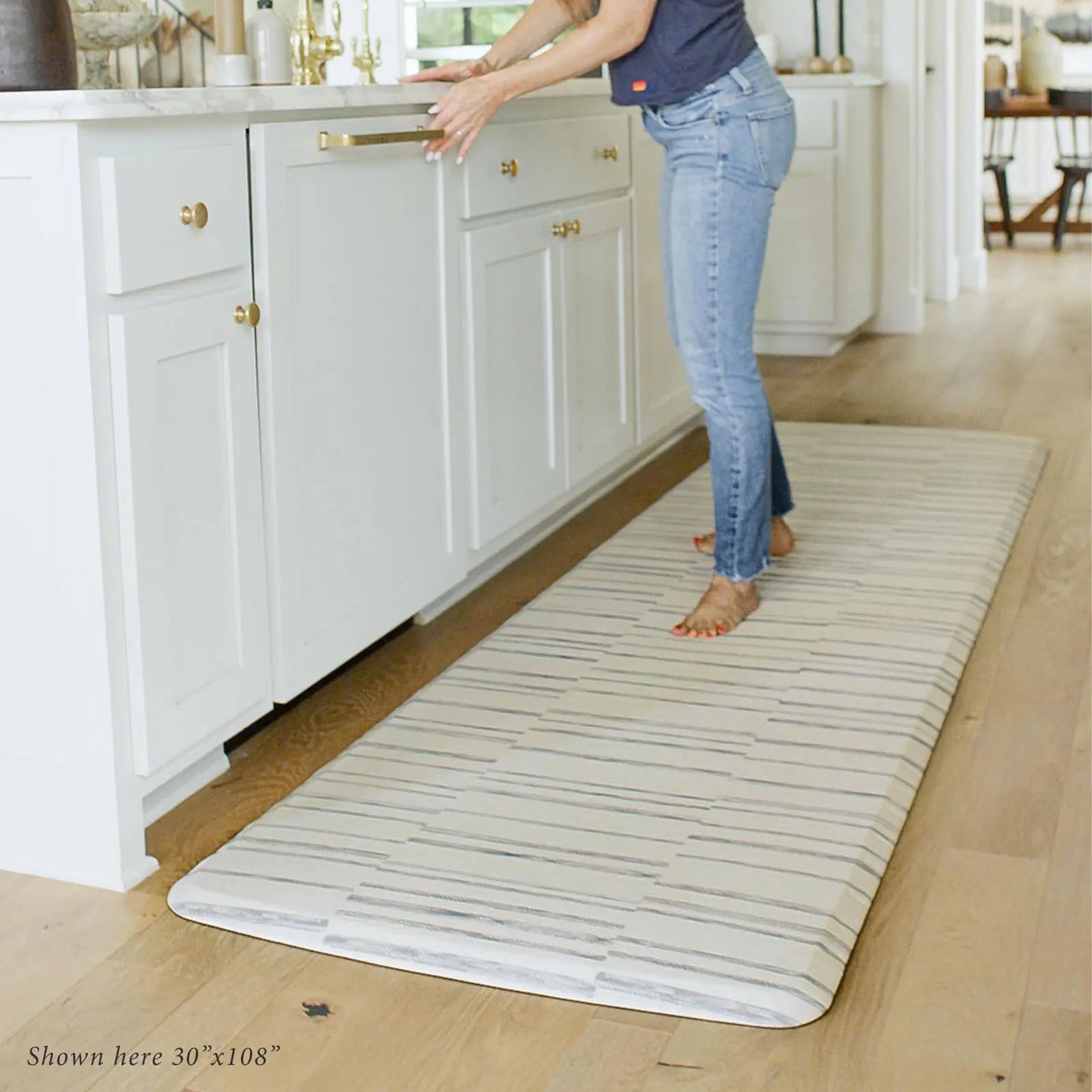 Gray and white inverted stripe kitchen mat in kitchen with woman closing dishwasher standing on size 30x108.