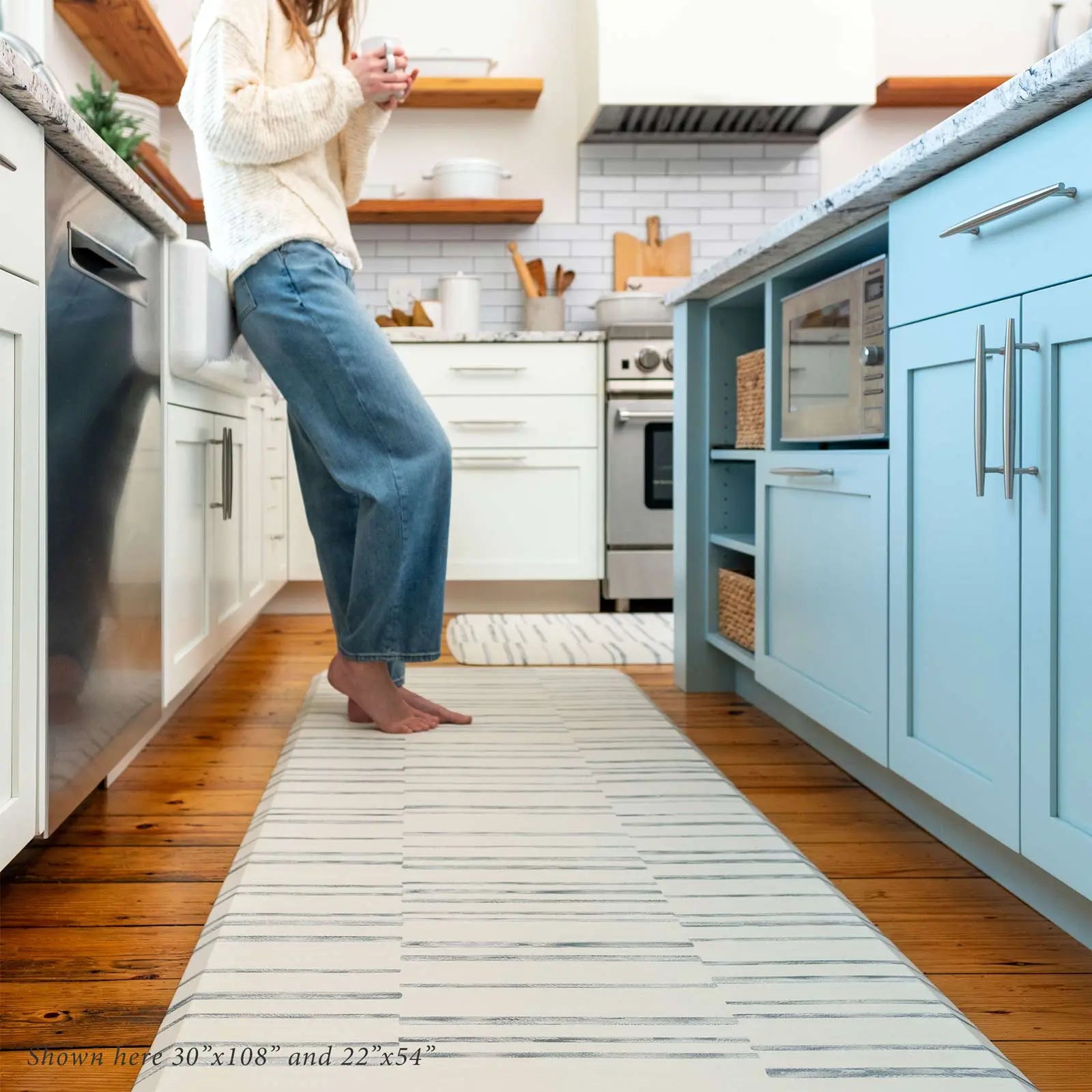 Gray and white inverted stripe kitchen mat shown with woman in kitchen drinking a cup of coffee standing on size 30x108