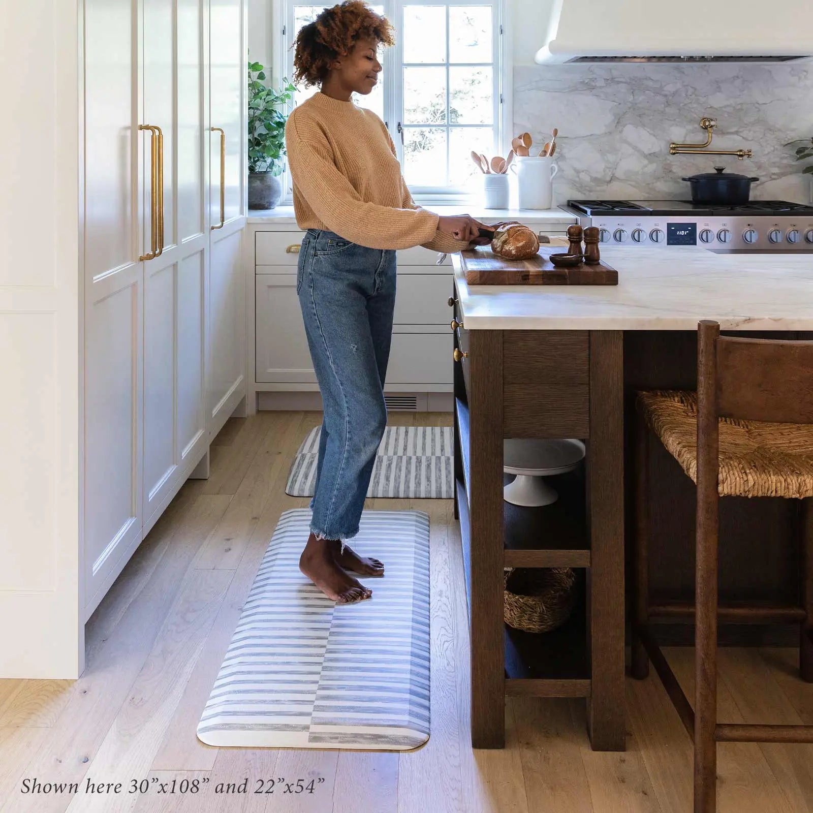 Reese pewter gray and white inverted stripe standing mat shown in kitchen in sizes 22x54 and 30x108 with woman cutting bread