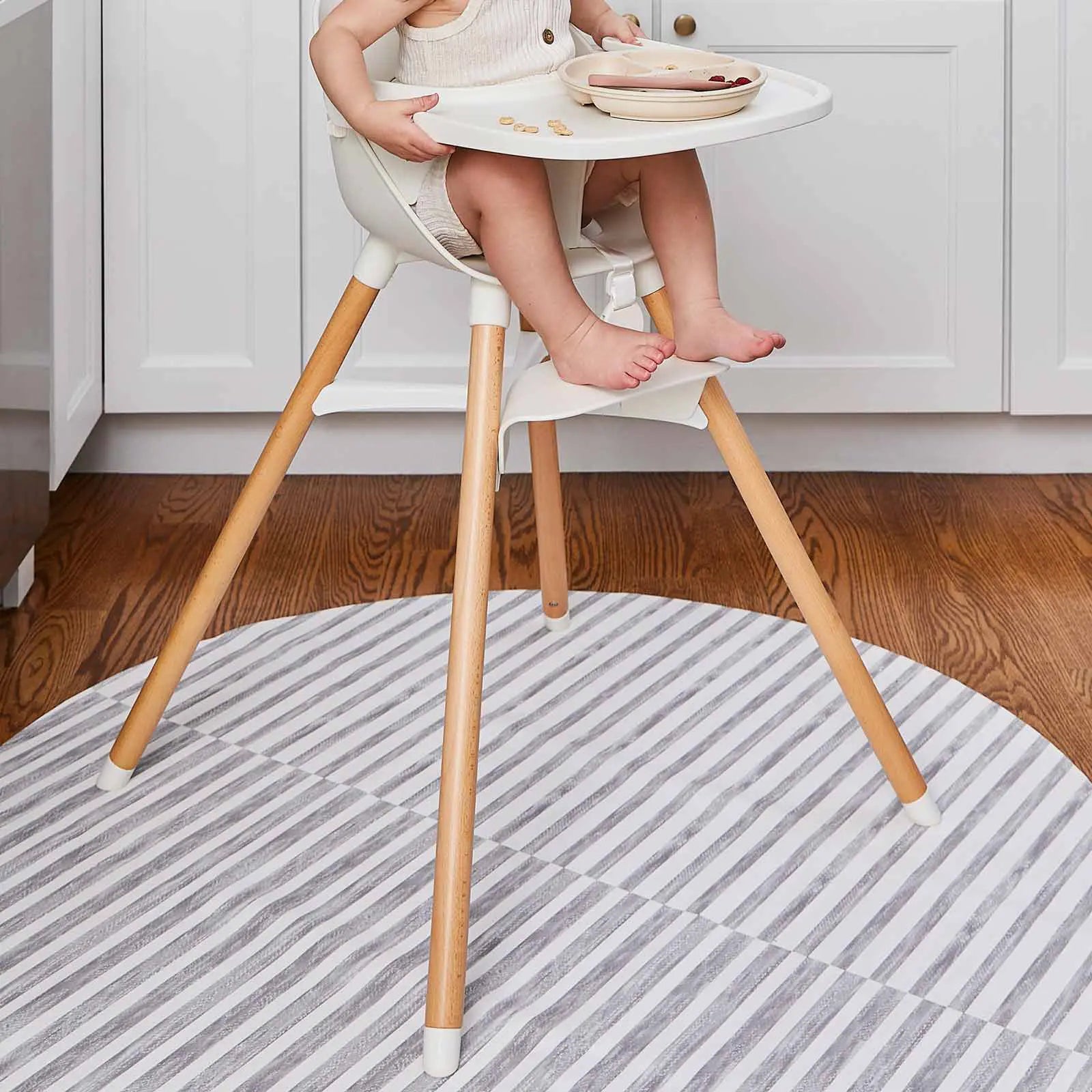 Reese pewter gray and white inverted stripe high chair mat shown in a kitchen under a highchair mat with toddler sitting in the chair eating