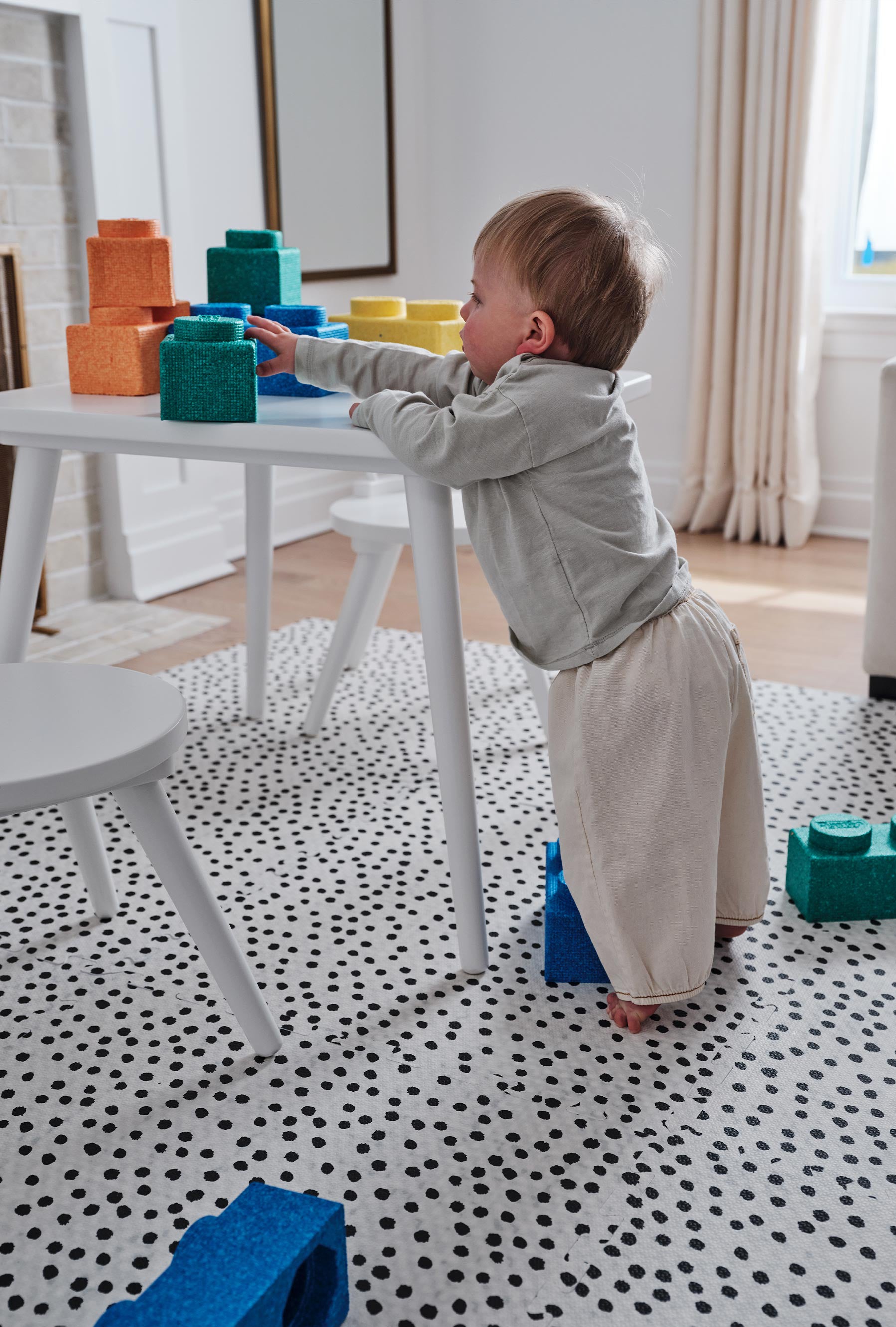 Apollo pepper black and white polka dot play mat shown in living room with baby putting large lego blocks on play table