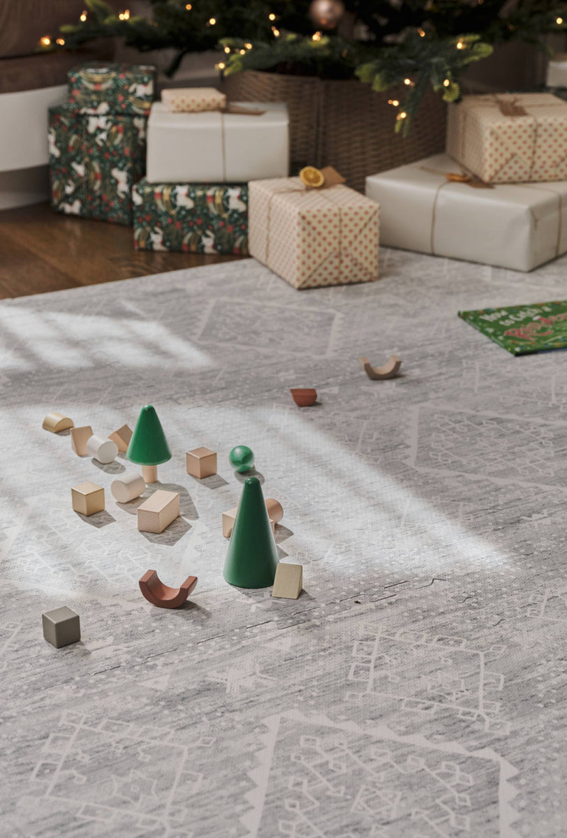Ula gray boho play mat shown in front of a christmas tree and wrapped presents with wooden blocks on the mat