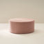 A pink boucle ottoman on a light background, with a textured surface and a round shape.