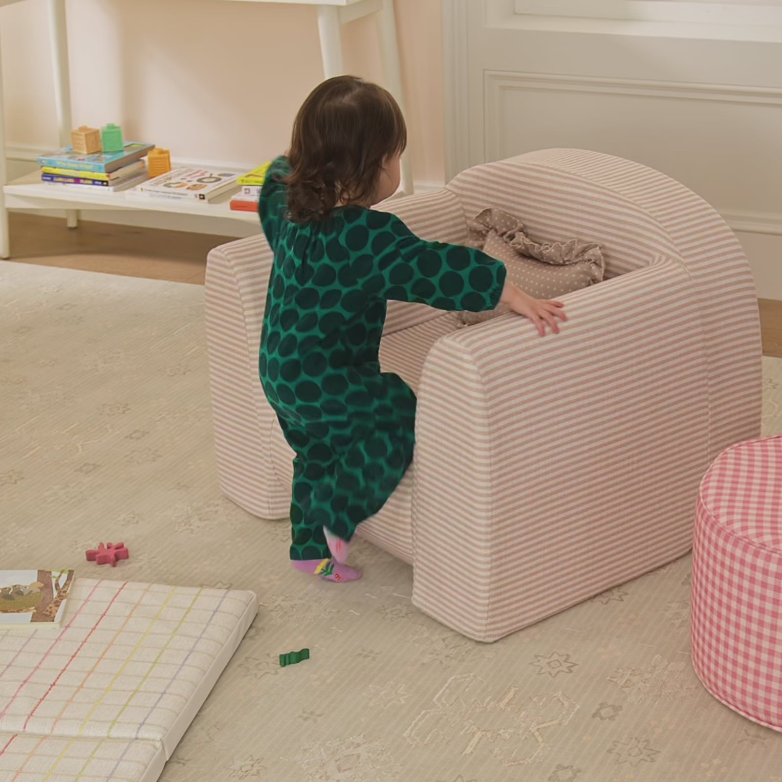 Child climbing in and out of pink and white striped play chair with ruffle pillow on a patterned play mat