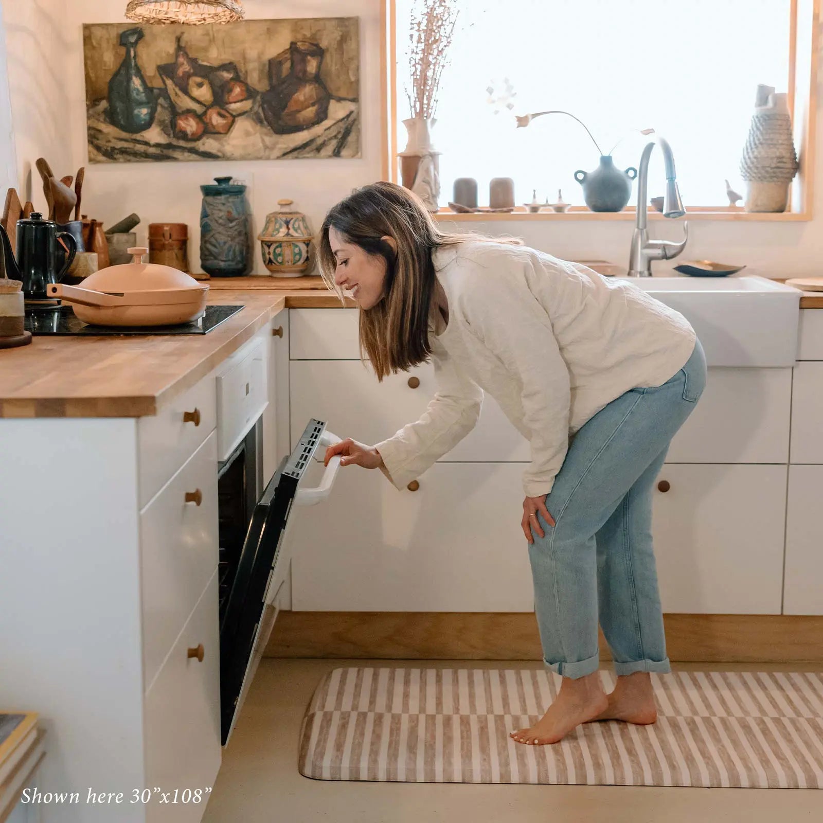 Reese chai beige and white inverted stripe standing mat shown in kitchen in size 30x108 with woman standing on mat opening the oven