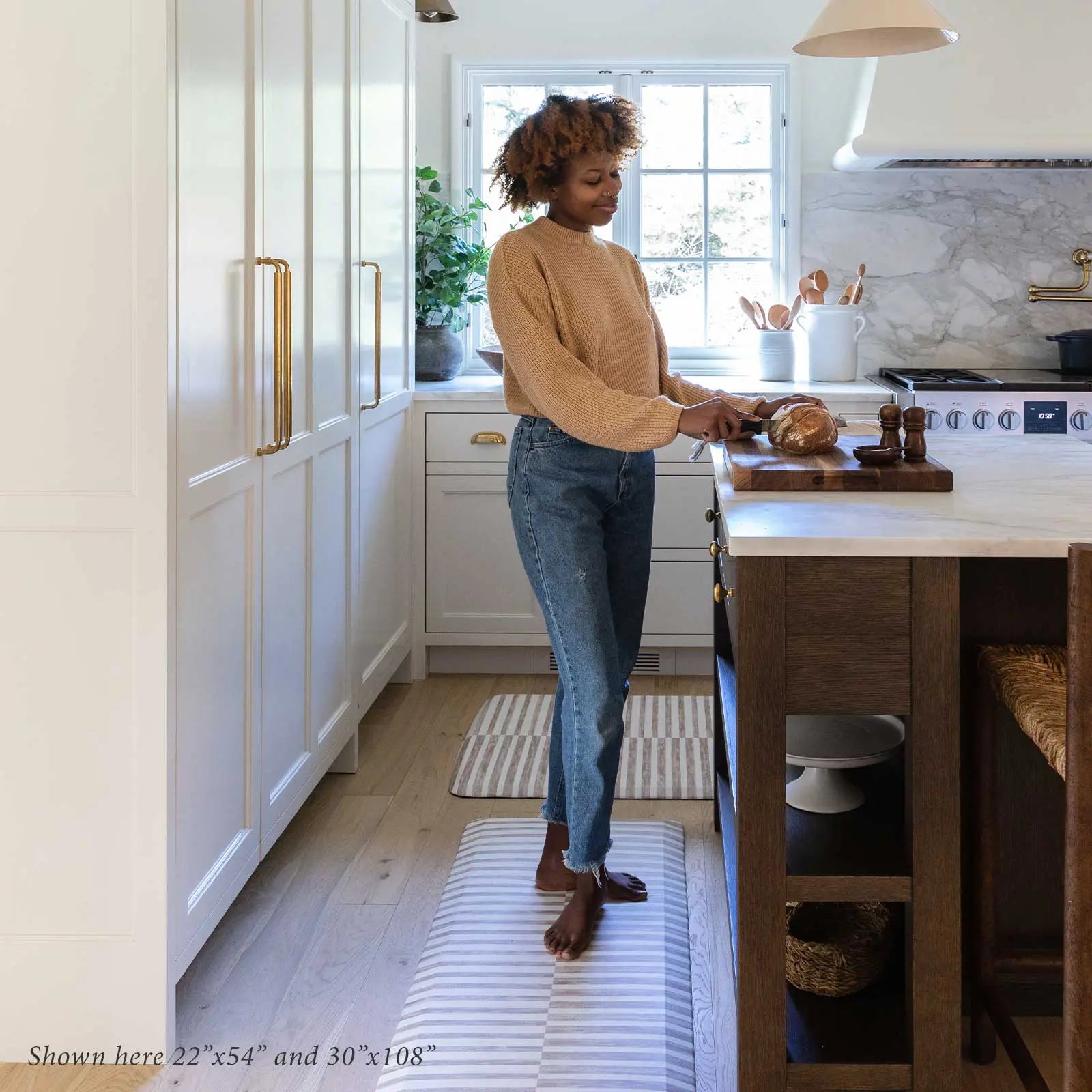 Reese chai beige and white inverted stripe standing mat shown in kitchen with woman cutting bread with sizes 22x54 and 30x108