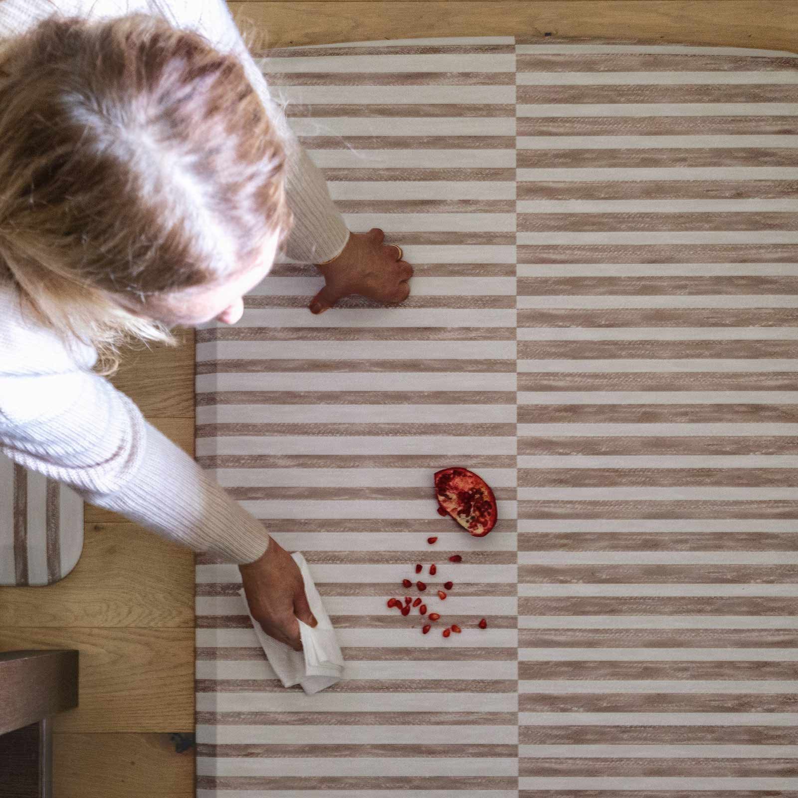 Reese chai beige and white inverted stripe standing mat shown from above with woman wiping up a spill