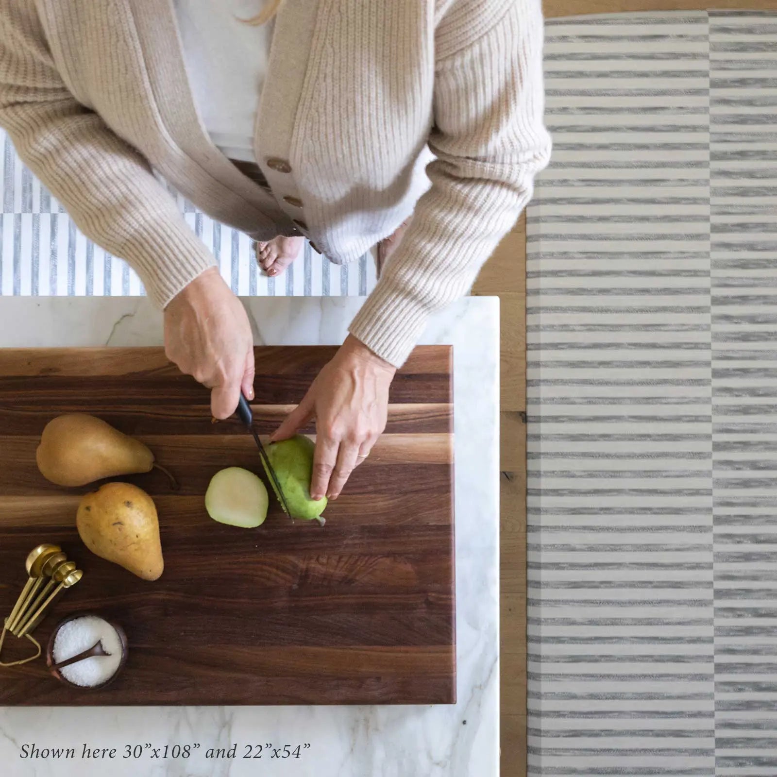 Reese pewter gray and white inverted stripe standing mat shown from above in kitchen in sizes 22x54 and 30x108 with woman cutting pears