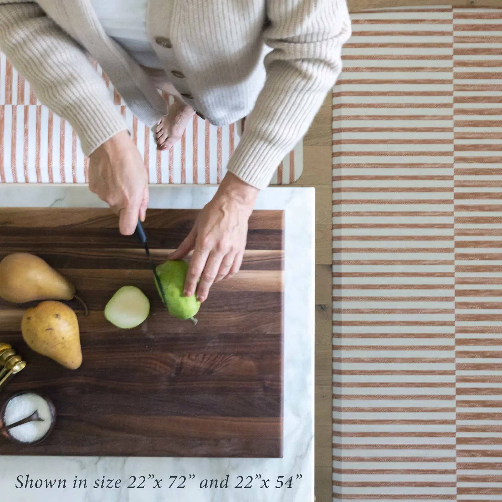 Reese terracotta brown and white inverted stripe standing mat shown from above in kitchen in sizes 22x54 and 22x72 with woman cutting pears