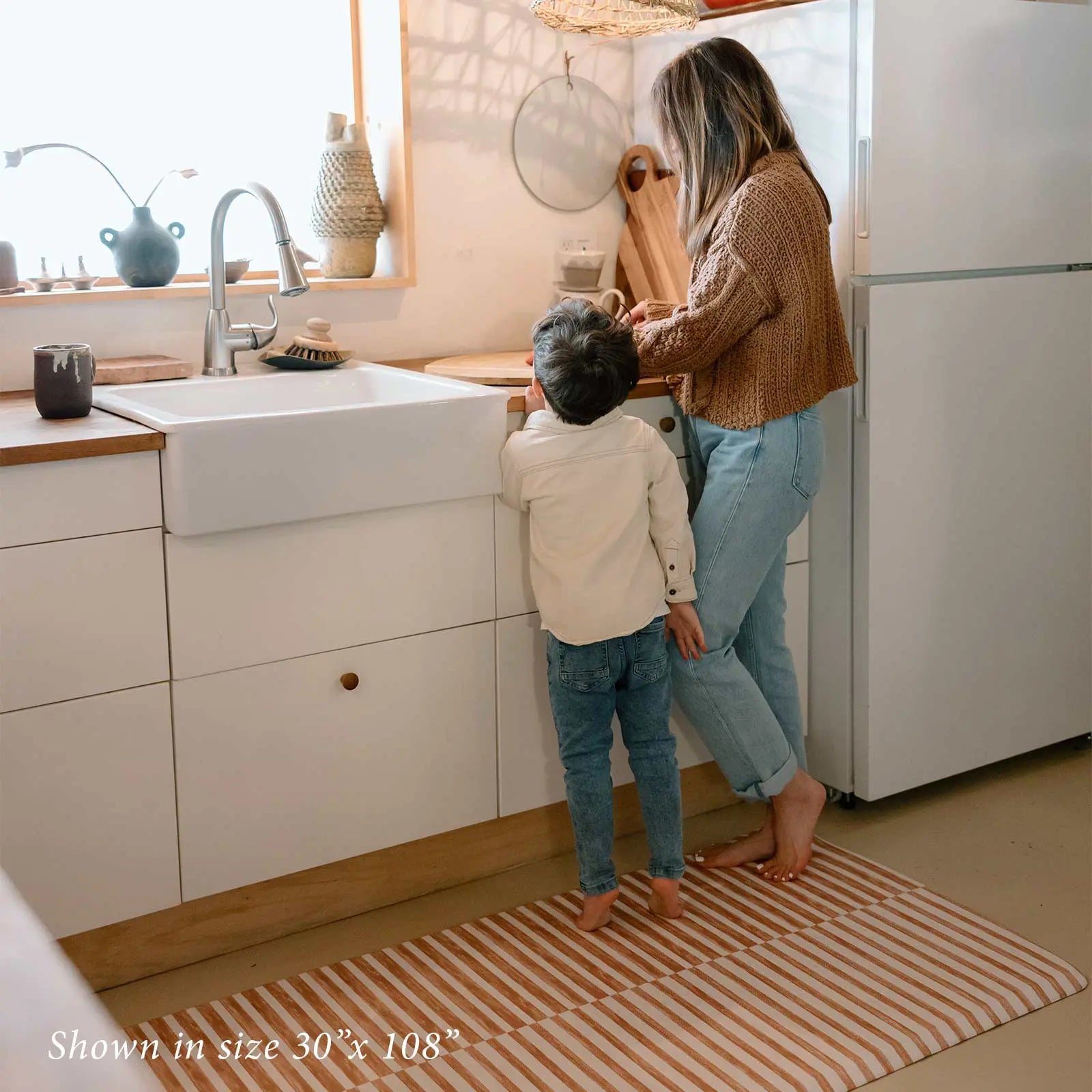Reese terracotta brown and white inverted stripe standing mat shown in kitchen in size 30x108 with Mom and son cooking