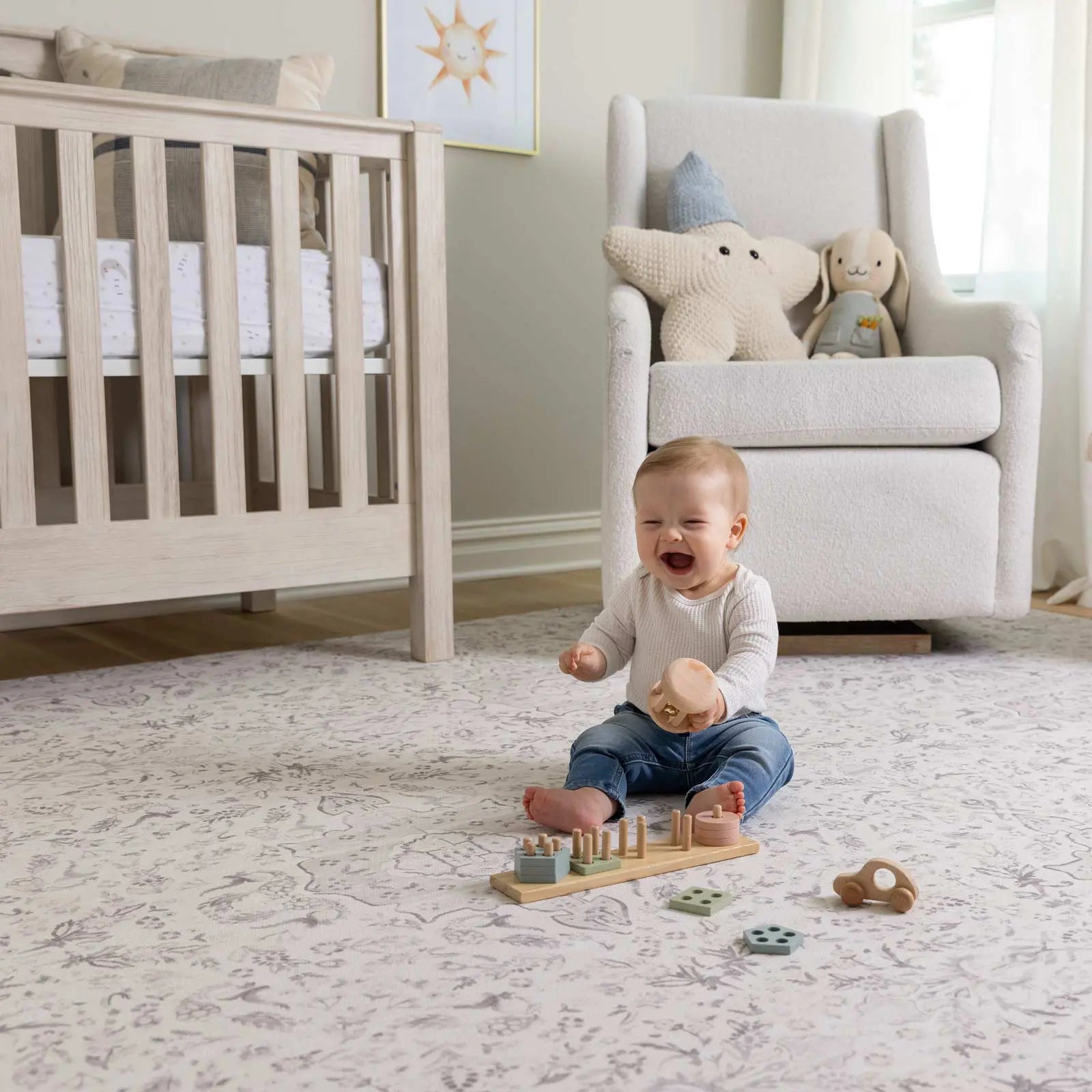 Emile latte neutral floral play mat shown in nursery with baby sitting on mat playing with wooden toys and laughing shaking his hands