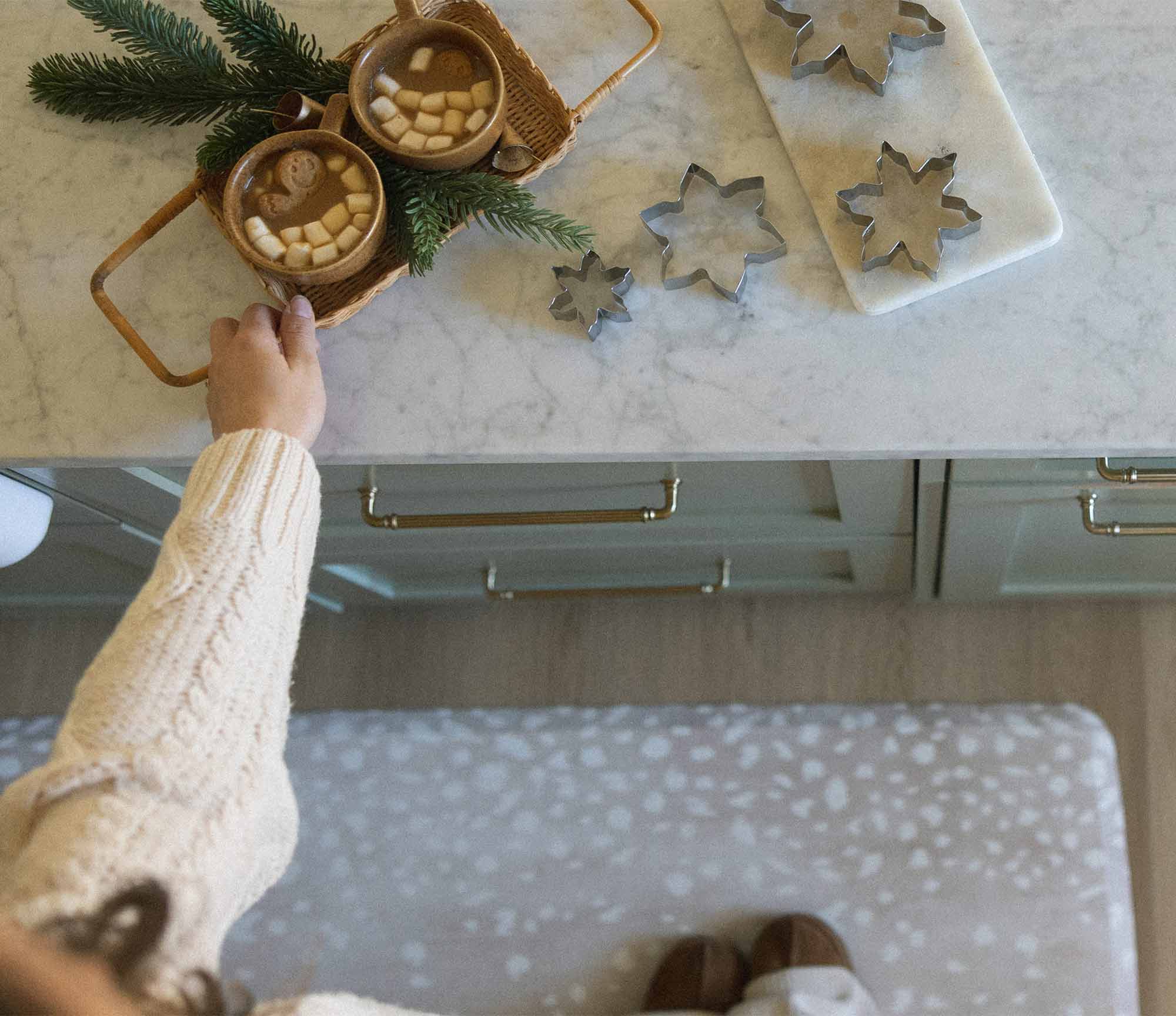 Fawn silver gray animal print kitchen mat shown in front of kitchen counter with woman reaching for cookie cutters and hot cocoa