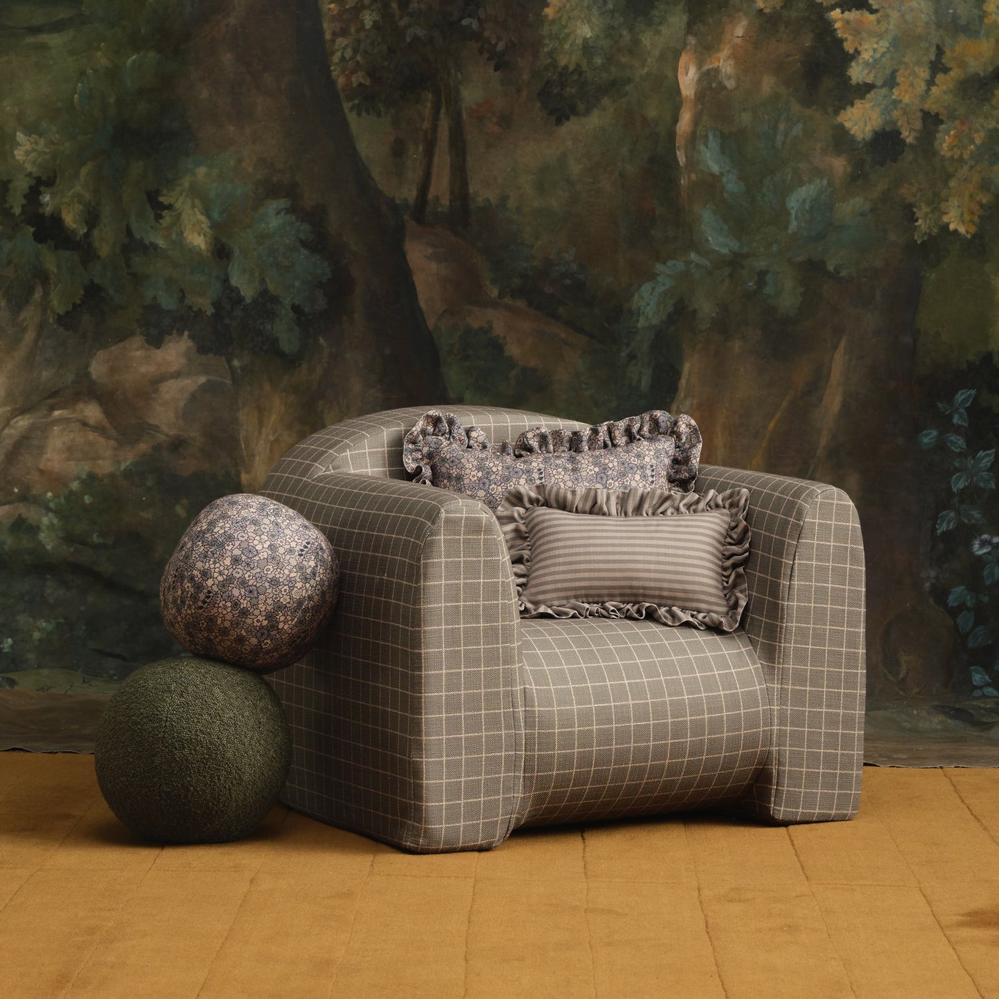 Gray checkered armchair with decorative pillows in a room with a forest mural.