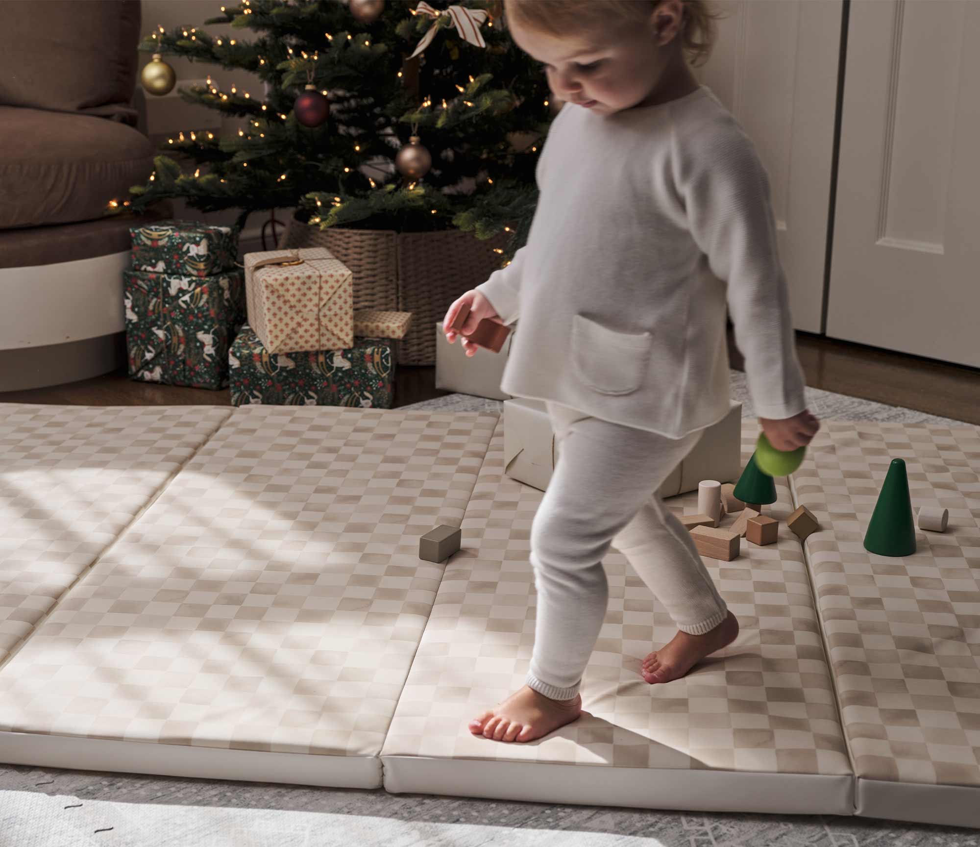 Checker Almond cream and brown geometric print tumbling mat shown with toddler walking across the mat with wooden blocks scattered