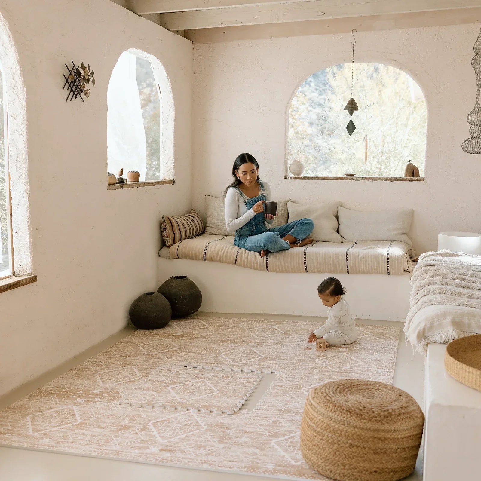 Ula Amber brown minimal boho pattern play mat shown in living room with one tile exposed and Mom watching baby play with wooden toys
