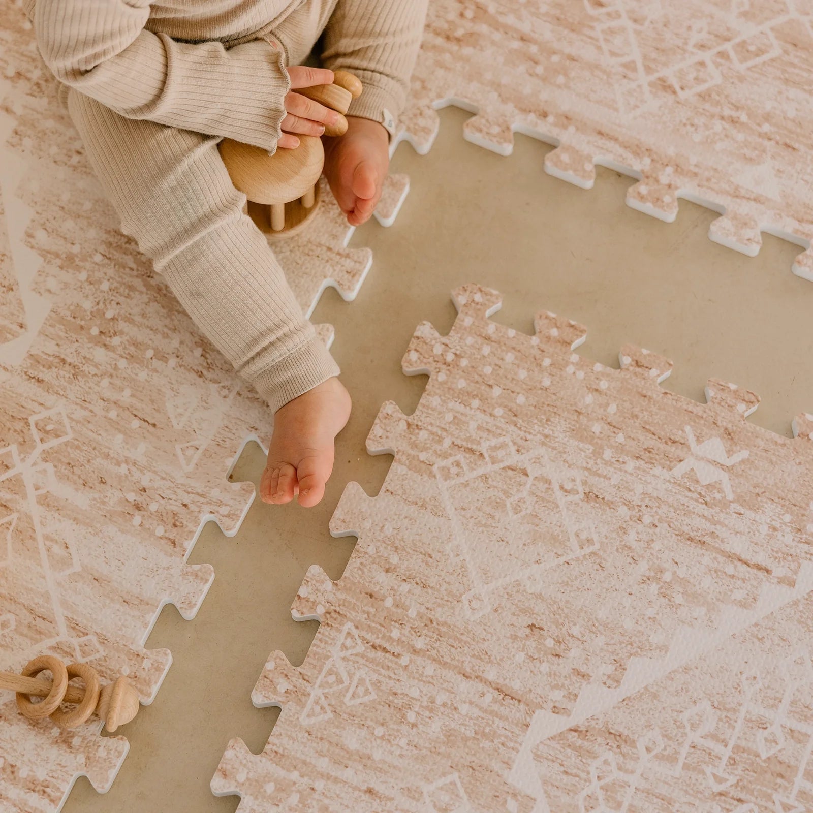 Ula Sienna neutral pink minimal boho pattern play mat shown close up with 1 tile exposed and babies feet and hands playing with wooden toys