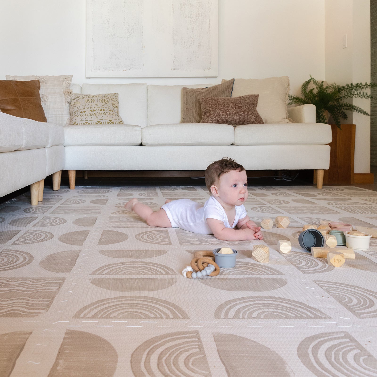 Ada modern minimalist baby play mat in Pebble taupe and off white. Shown in living room with baby playing with toys.