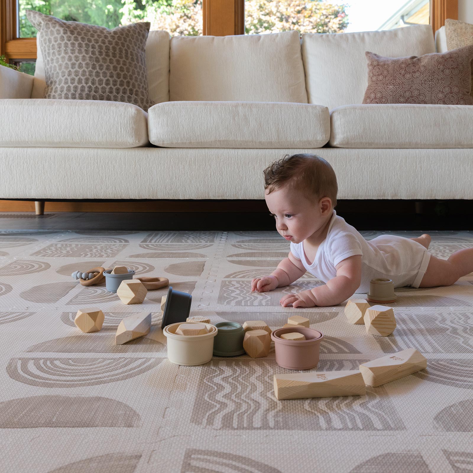 Ada modern minimalist baby play mat in Pebble taupe and off white. Shown in living room with baby playing with toys.