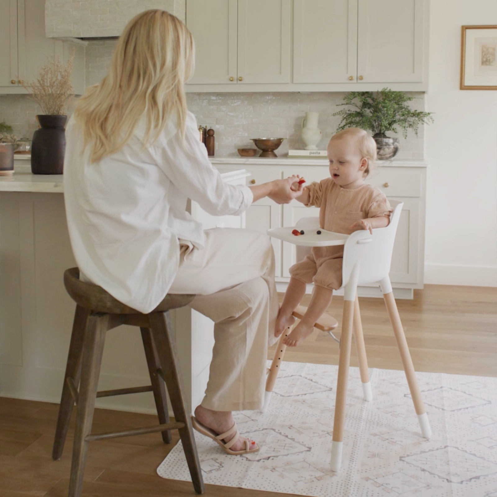 Neutral boho baby highchair mat shown in kitchen with mom feeding baby