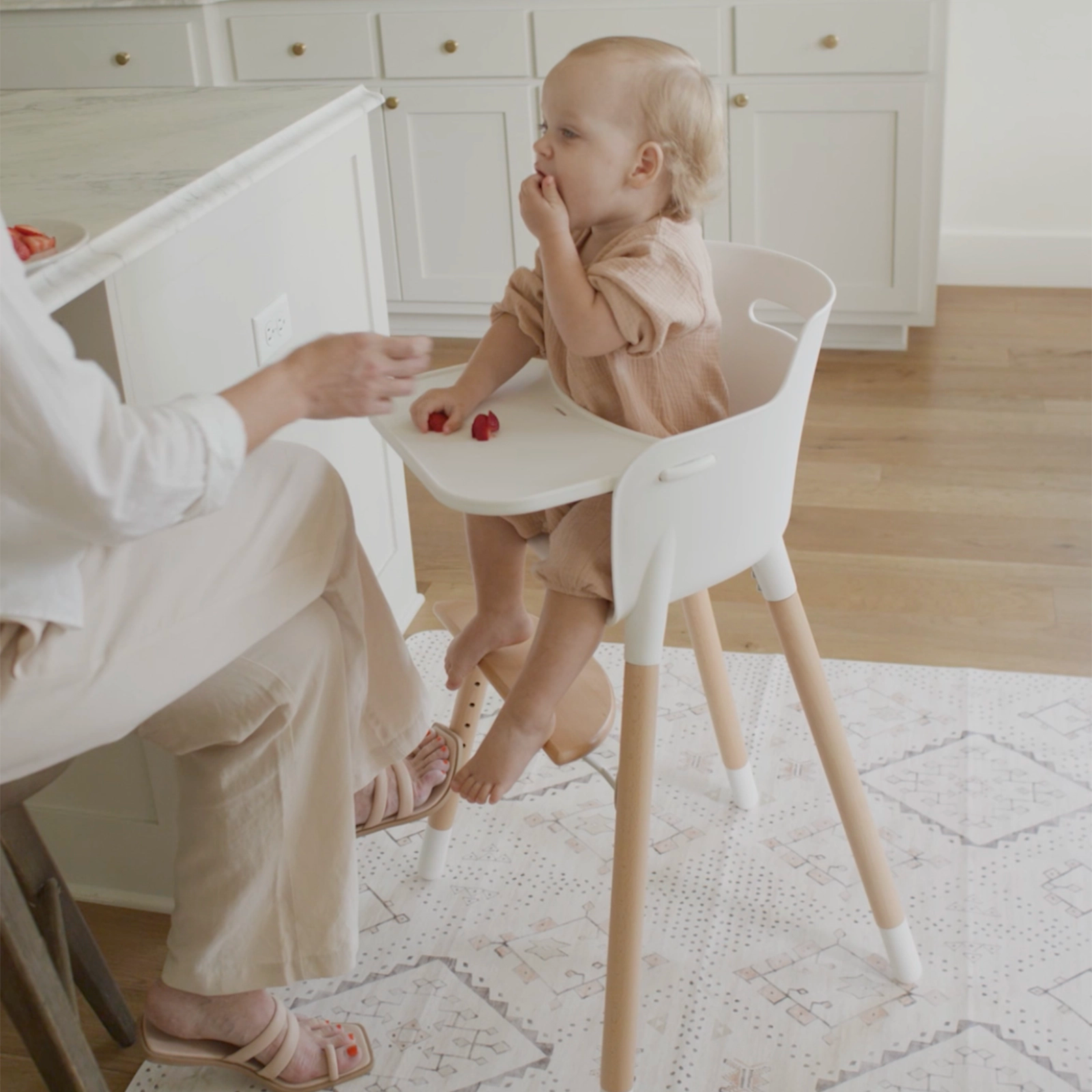 Neutral boho baby highchair mat shown in kitchen with mom feeding baby