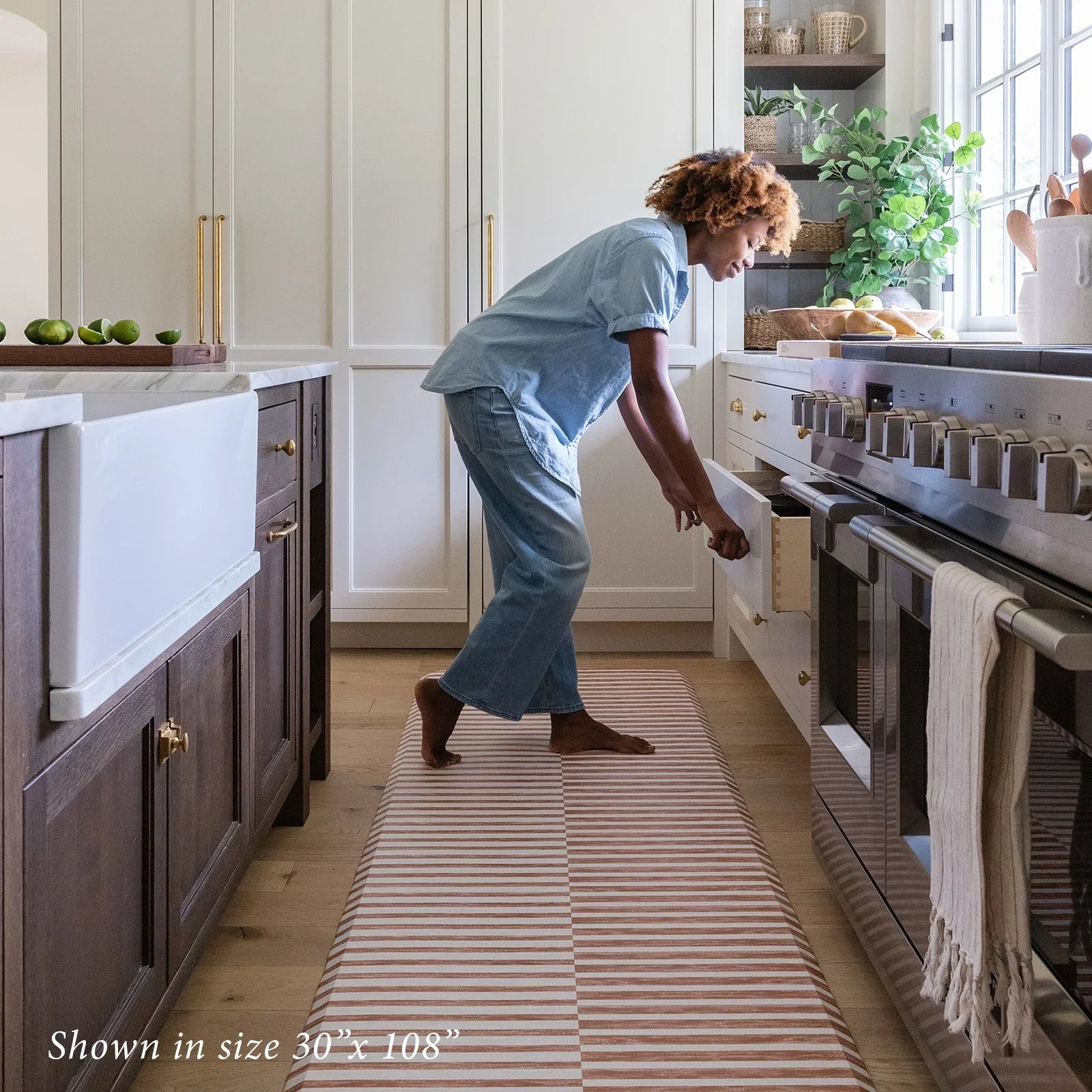 Reese terracotta brown and white inverted stripe standing mat shown in kitchen in size 30x108 with woman opening cabinet drawer
