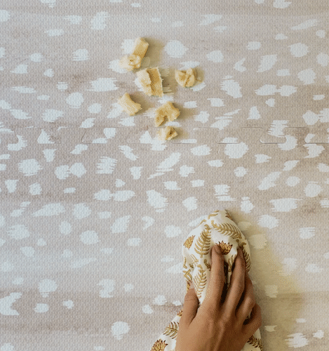 Fawn neutral beige animal print baby play mat. Moving GIF image shot from above with hand wiping up food spill.