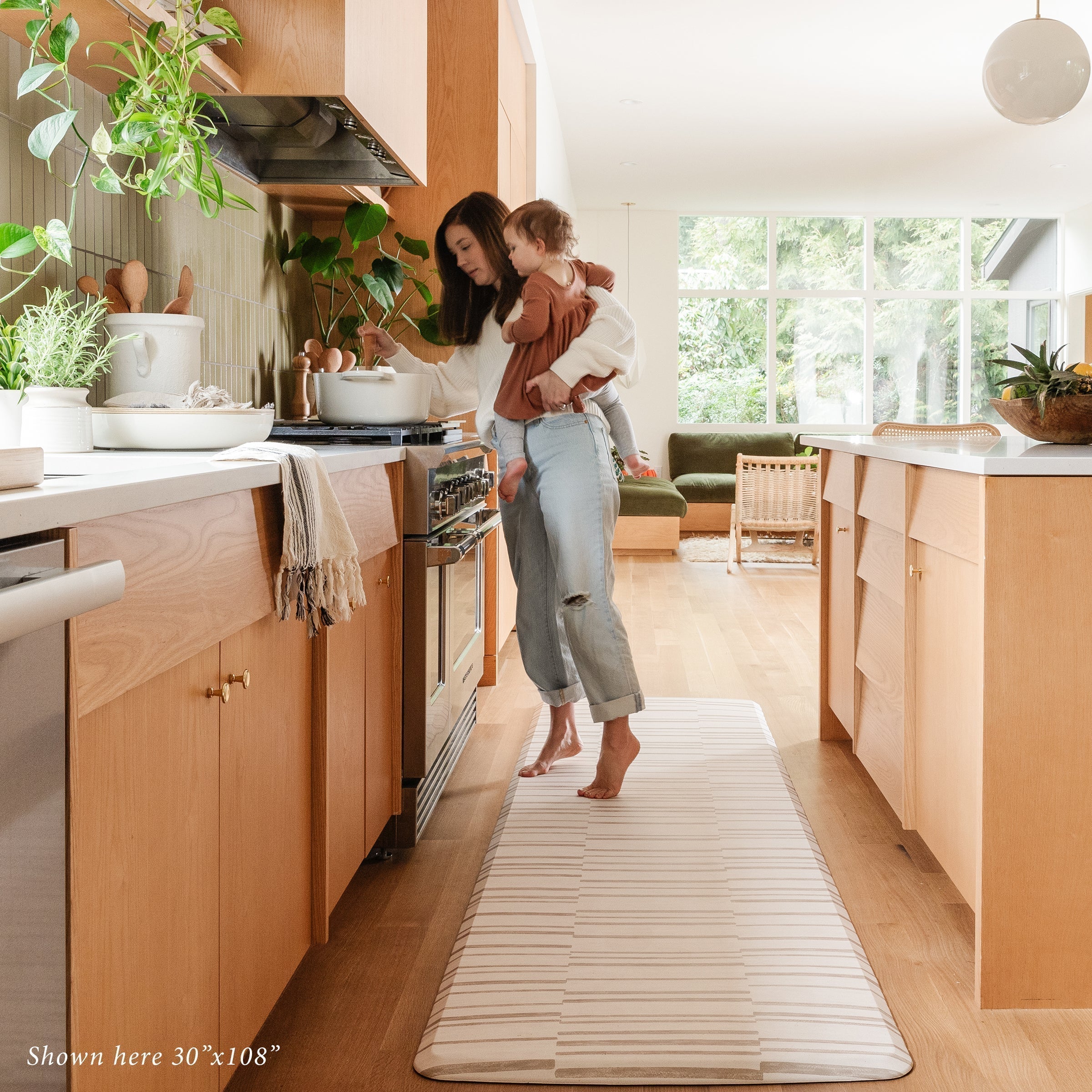 Beige inverted stripe kitchen mat in with Mom holding a baby cooking in kitchen on size 30x108.