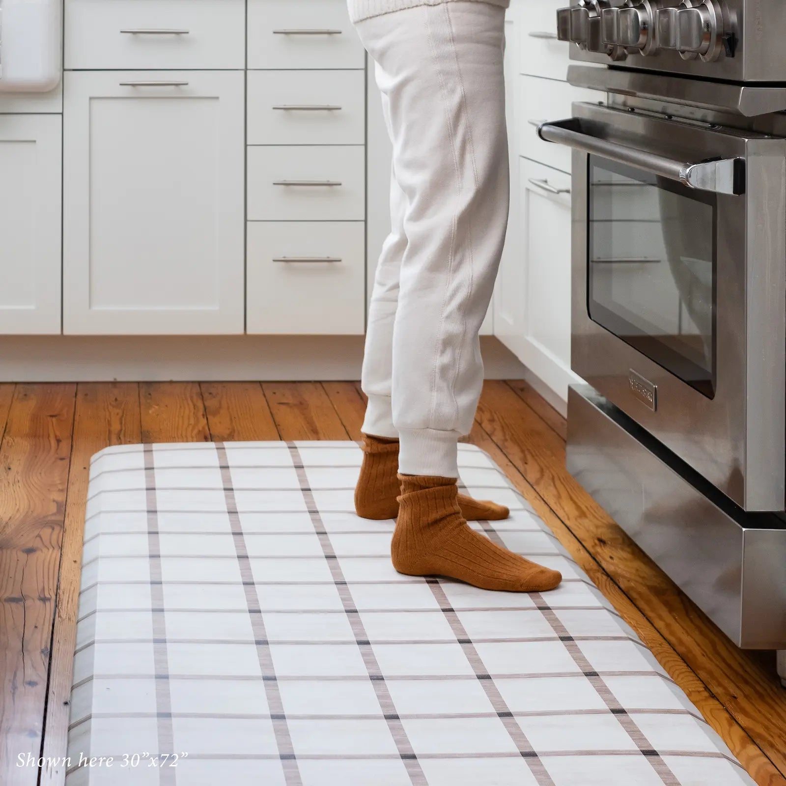 Brown and white neutral grid pattern kitchen mat shown with woman cooking at stove wearing white joggers and thick orange socks standing on size 30x72