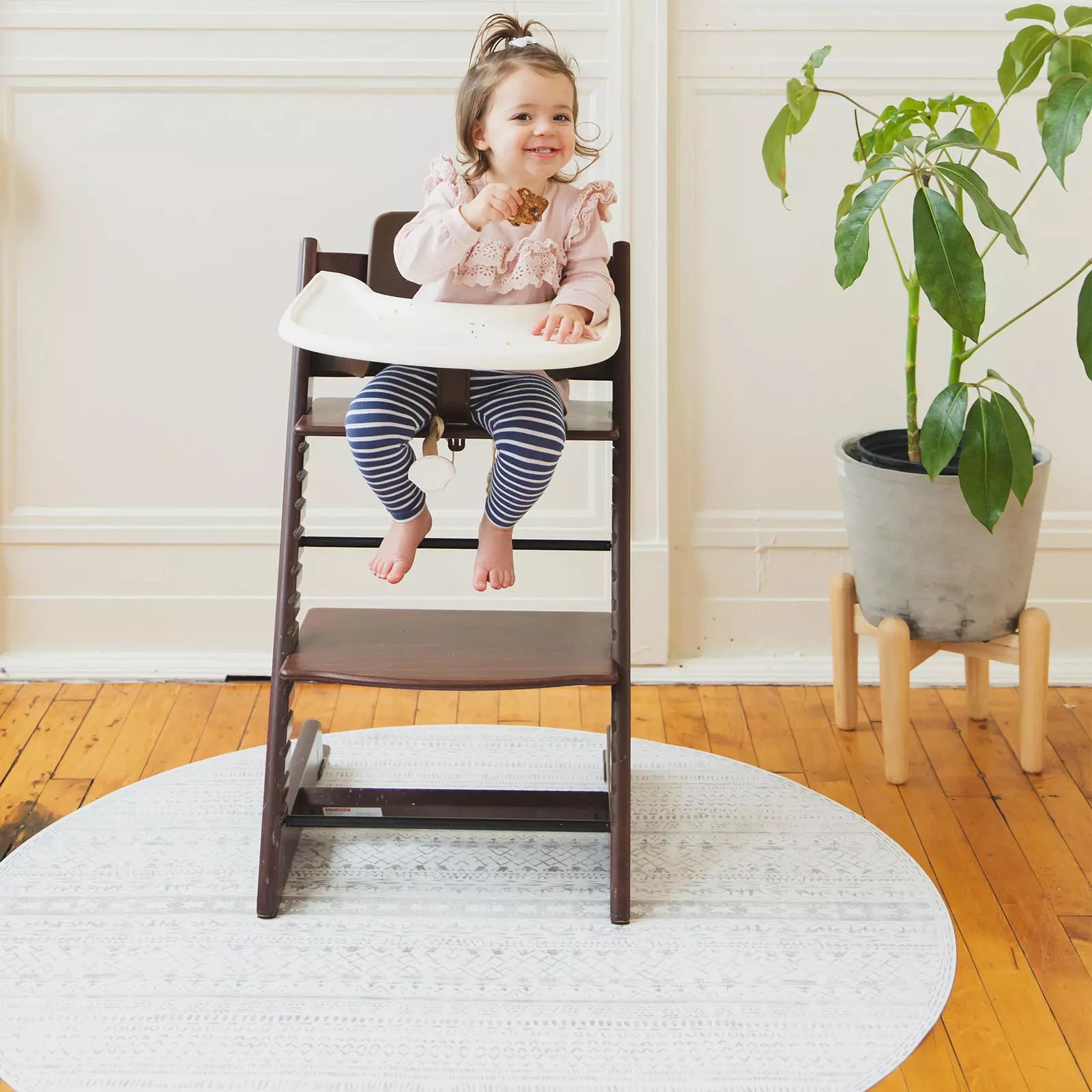 Skipping Stone gray and white striped highchair mat shown under highchair with baby eating